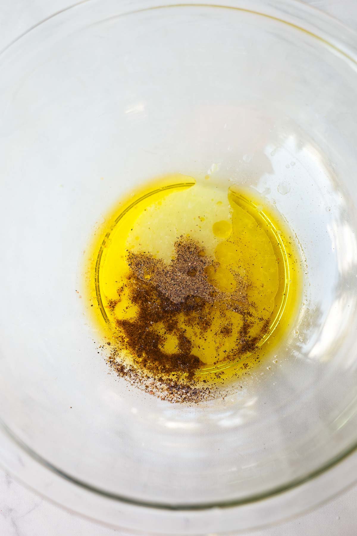 glass mixing bowl with olive oil, lime juice, salt, and pepper.