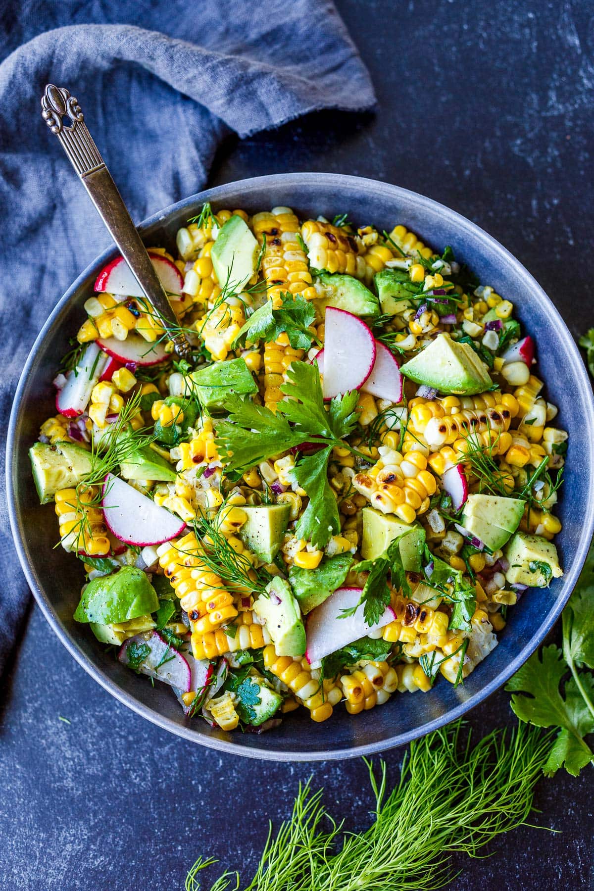 bowl with grilled corn salad with avocado and radish, garnished with cilantro and dill.