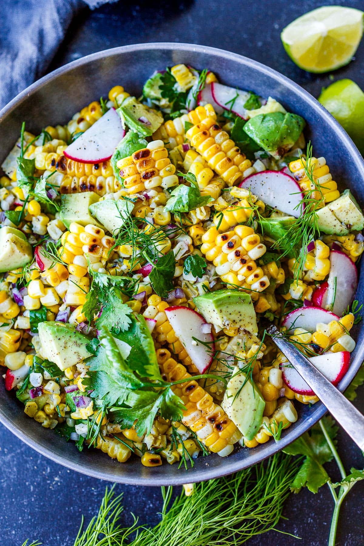 salad bowl with grilled corn salad and silver spoon, mixed with radish, avocado, minced red onion, cilantro, and dill.