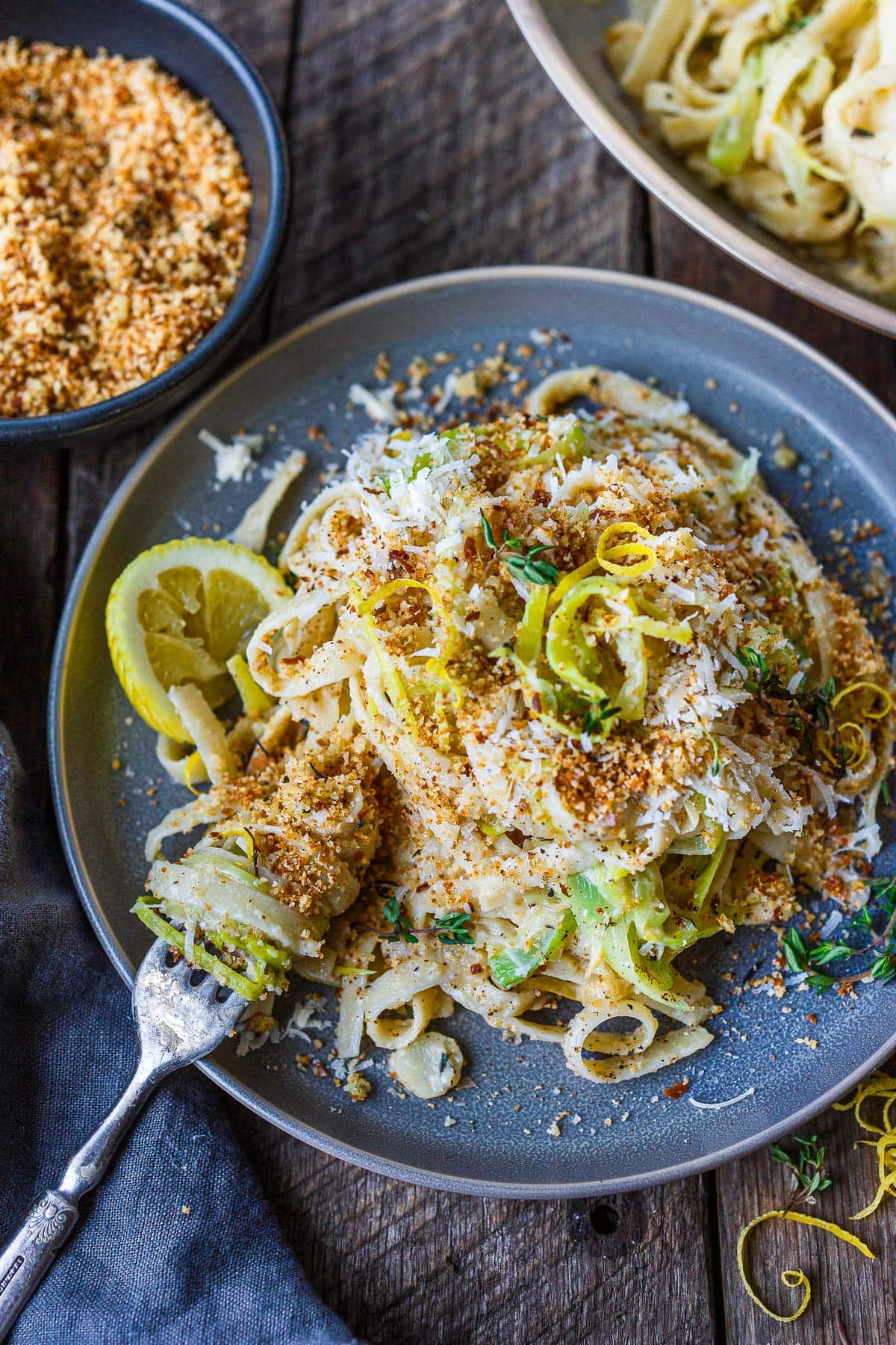 plate of caramelized leek pasta with fork twirling the noodles, garnished with toasted breadcrumbs, thyme, and lemon zest and wedge.