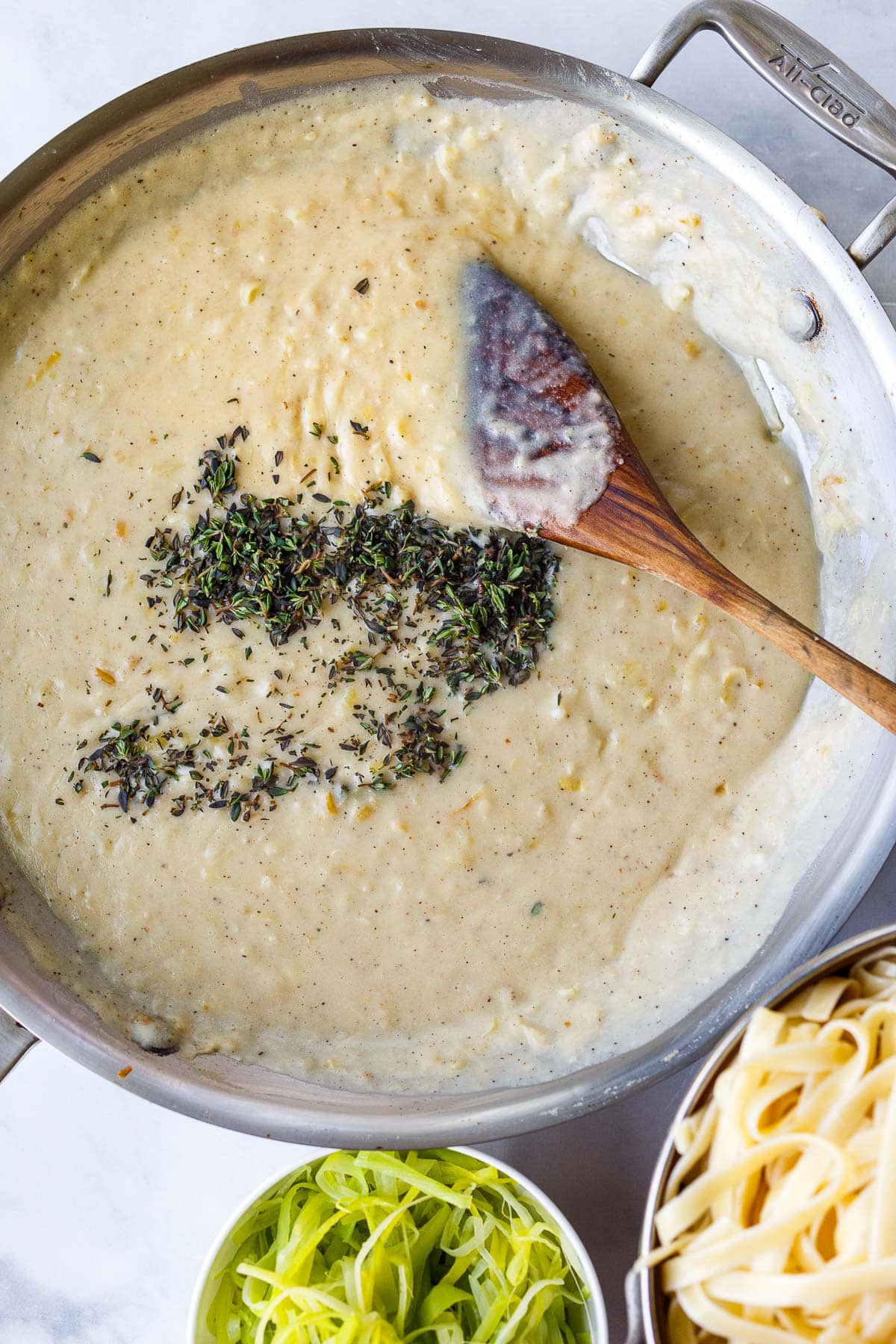 creamy caramelized leek pasta sauce in pan with wood spoon topped with fresh minced thyme.