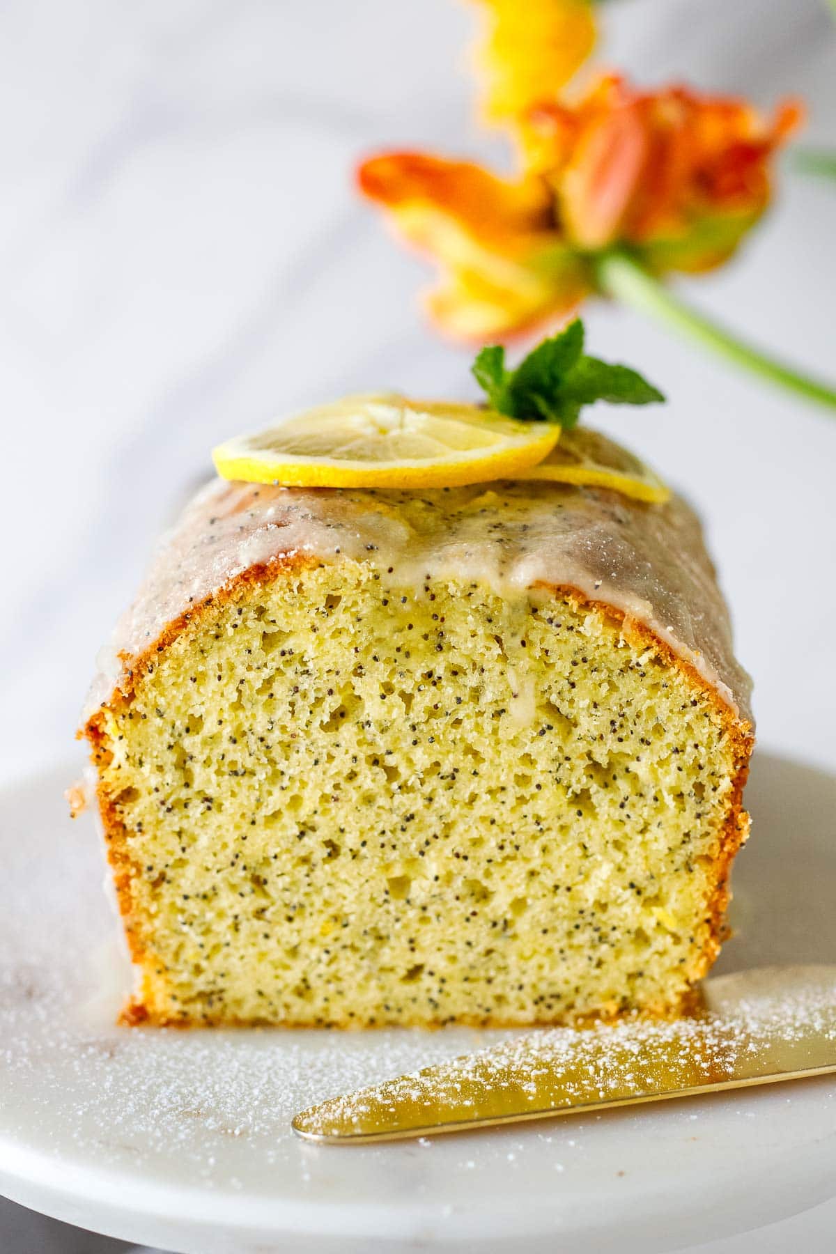 lemon poppy seed cake revealing interior, topped with lemon glaze, lemon slices, and mint leaves.