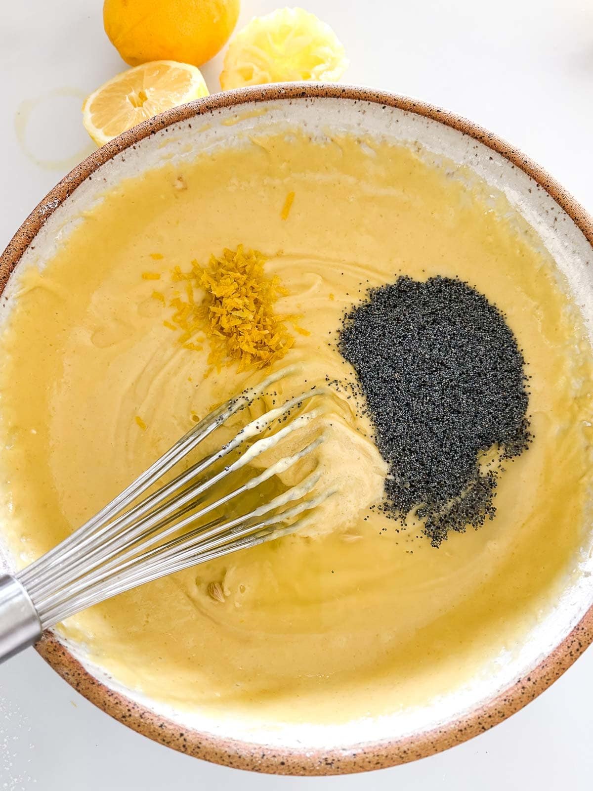 mixing bowl with lemon poppy seed cake batter with whisk stirring in poppy seeds and lemon zest.