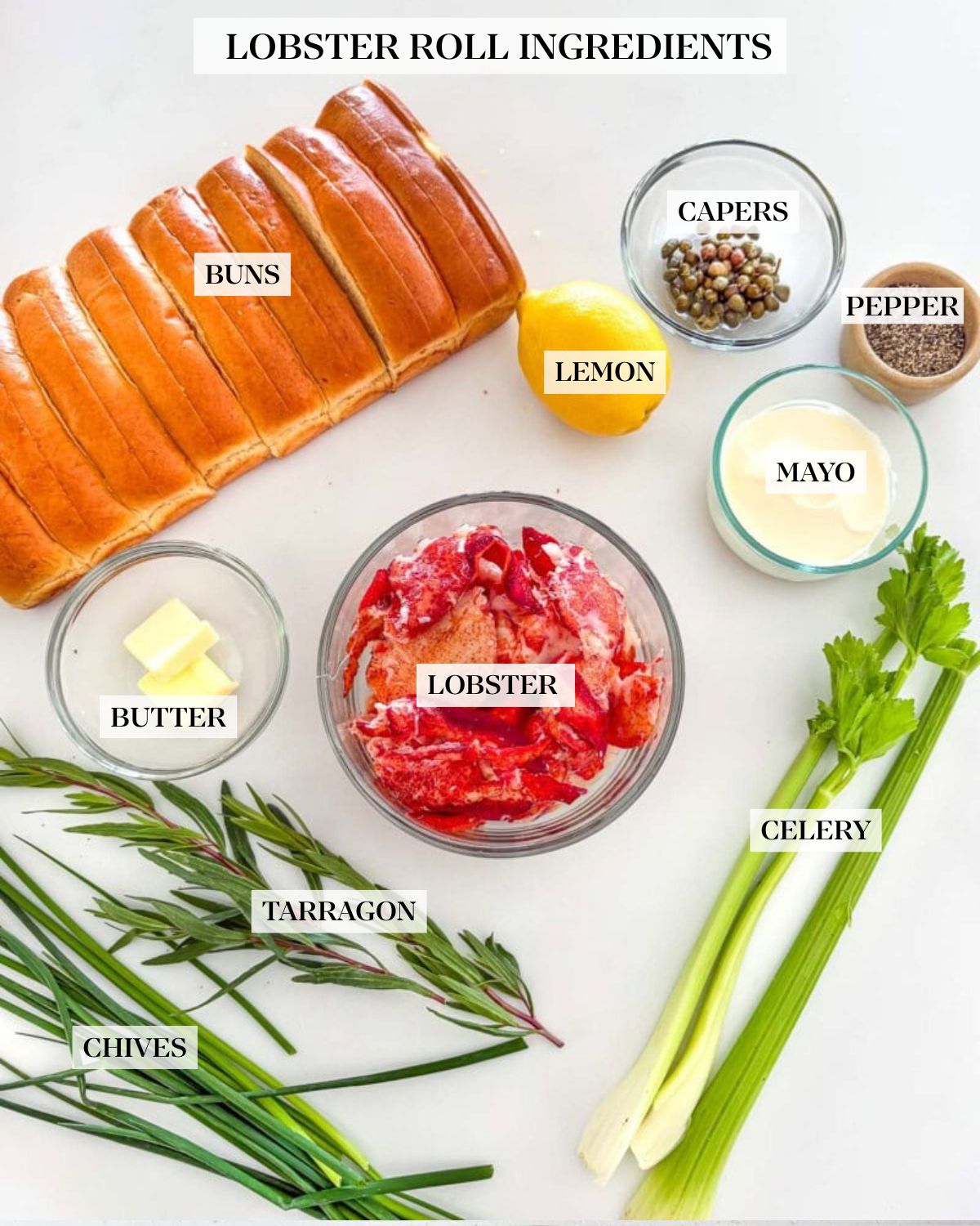 ingredients for lobster rolls arranged neatly - split-top buns, capers, lemon, mayonnaise, pepper, celery, lobster, butter, and herbs.