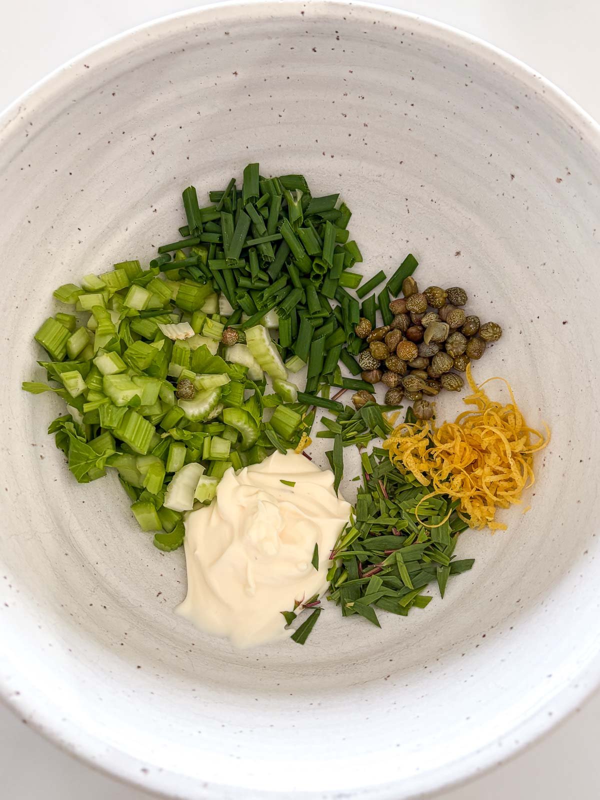 ceramic mixing bowl with celery, scallions, capers, lemon zest, tarragon, and mayonnaise.