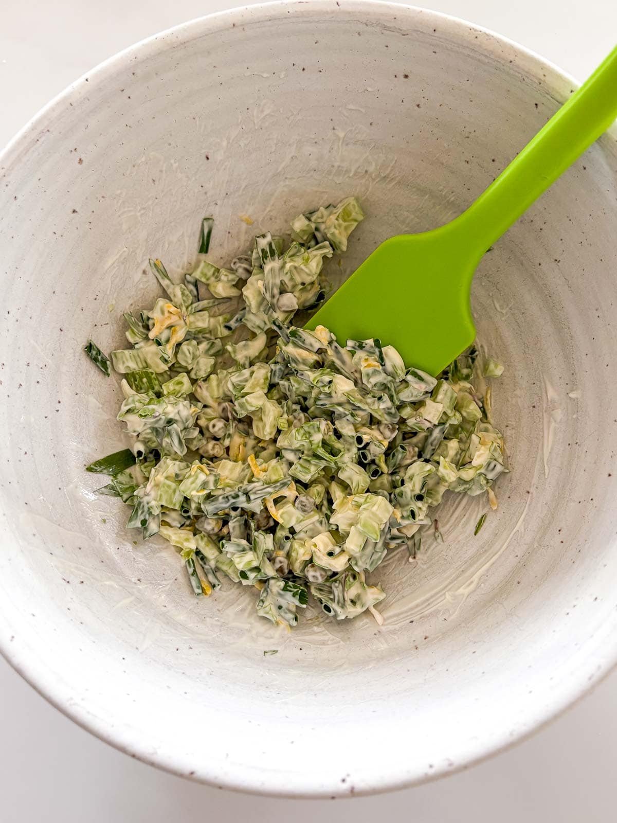 ceramic mixing bowl with mayo mixture being mixed with green silicone spatula.