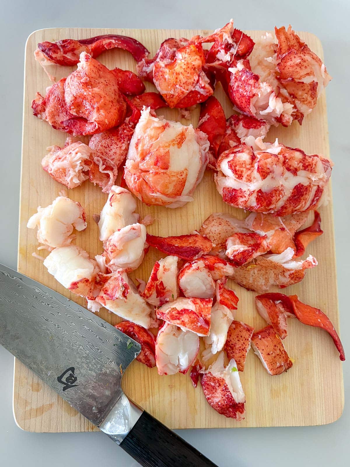 wood cutting board with torn apart lobster, shells and cartilage moved to the side, and sharp knife.