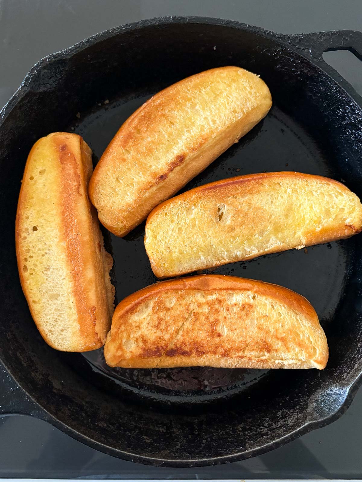 split-top buns toasting in butter in cast iron skillet.