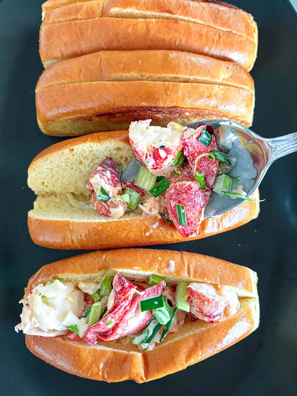spooning lobster rolls filling into toasted split-top buns.