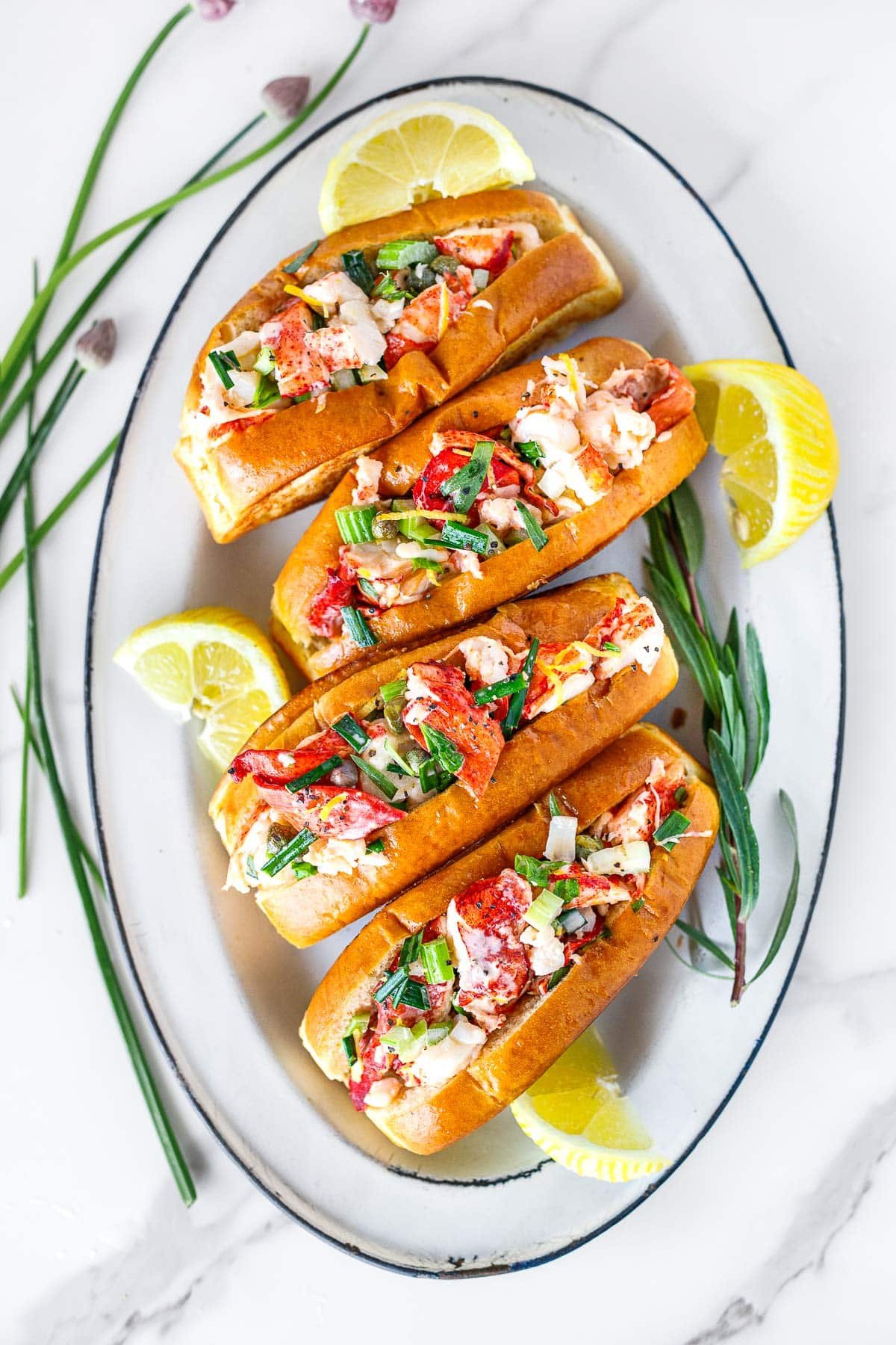 Maine-style lobster rolls in toasted split top buns on a white platter.