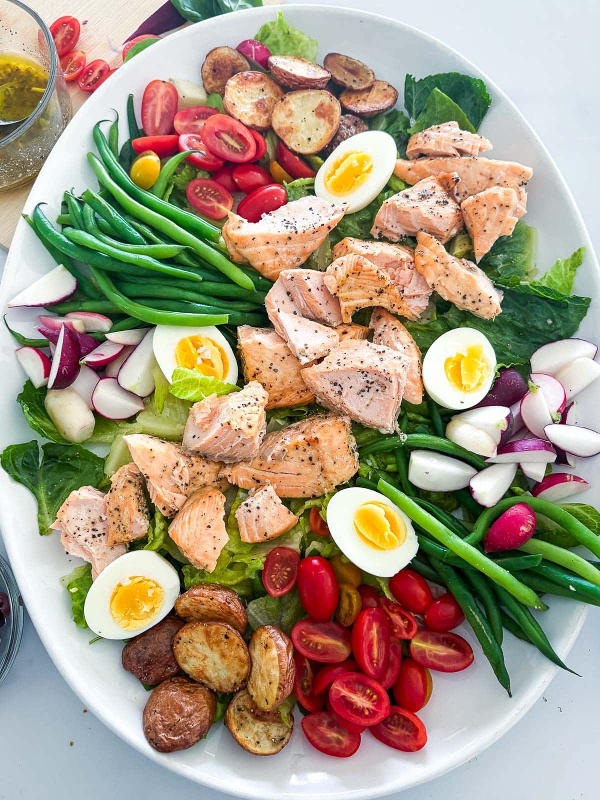 nicoise salad before dressing with baked salmon, boiled eggs, green beans, roasted potatoes, cherry tomatoes, and radishes over crisp greens.