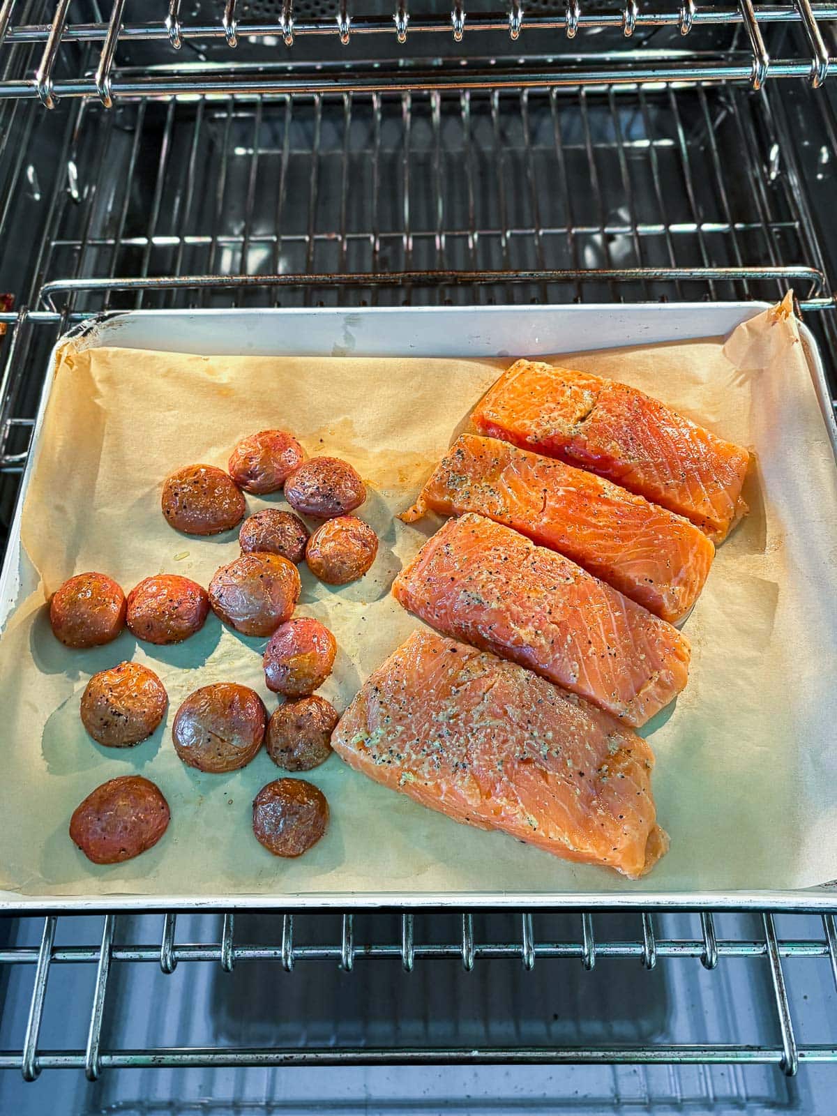 parchment lined baking sheet with roasted baby potatoes next to four seasoned salmon filets.