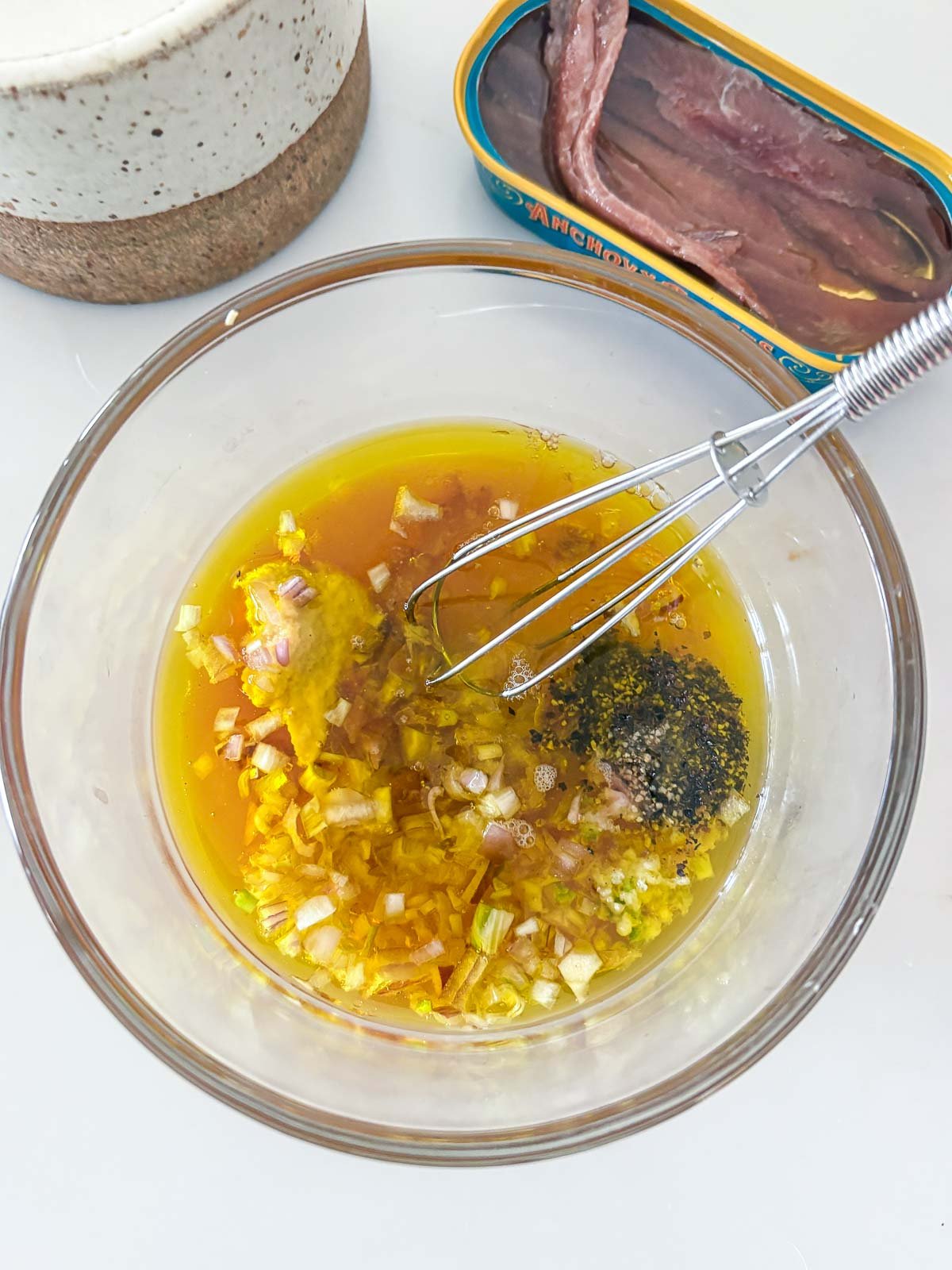 whisk and glass bowl mixing together dressing for nicoise salad.
