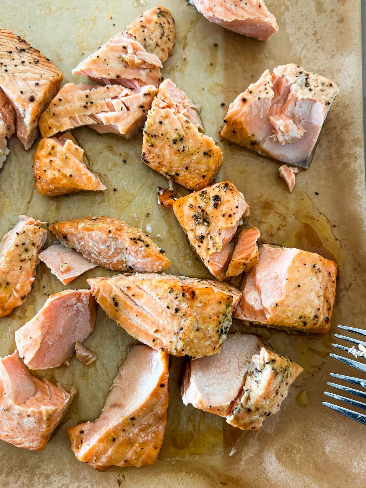 flaked baked dijon salmon with black pepper on parchment lined baking sheet with tips of forks.