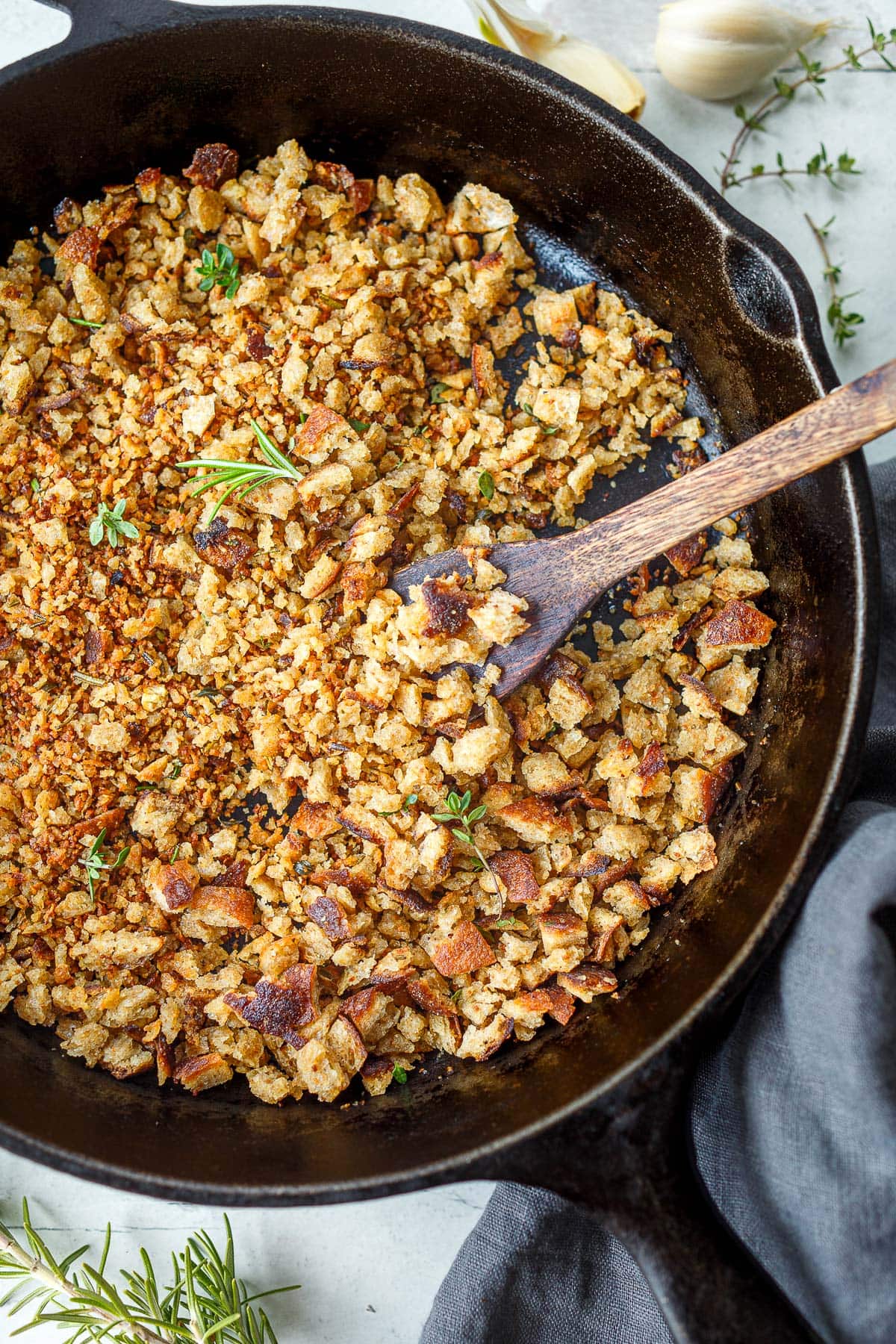 cast iron skillet with pangrattato topped with fresh herbs and with a wood spoon in the pan.