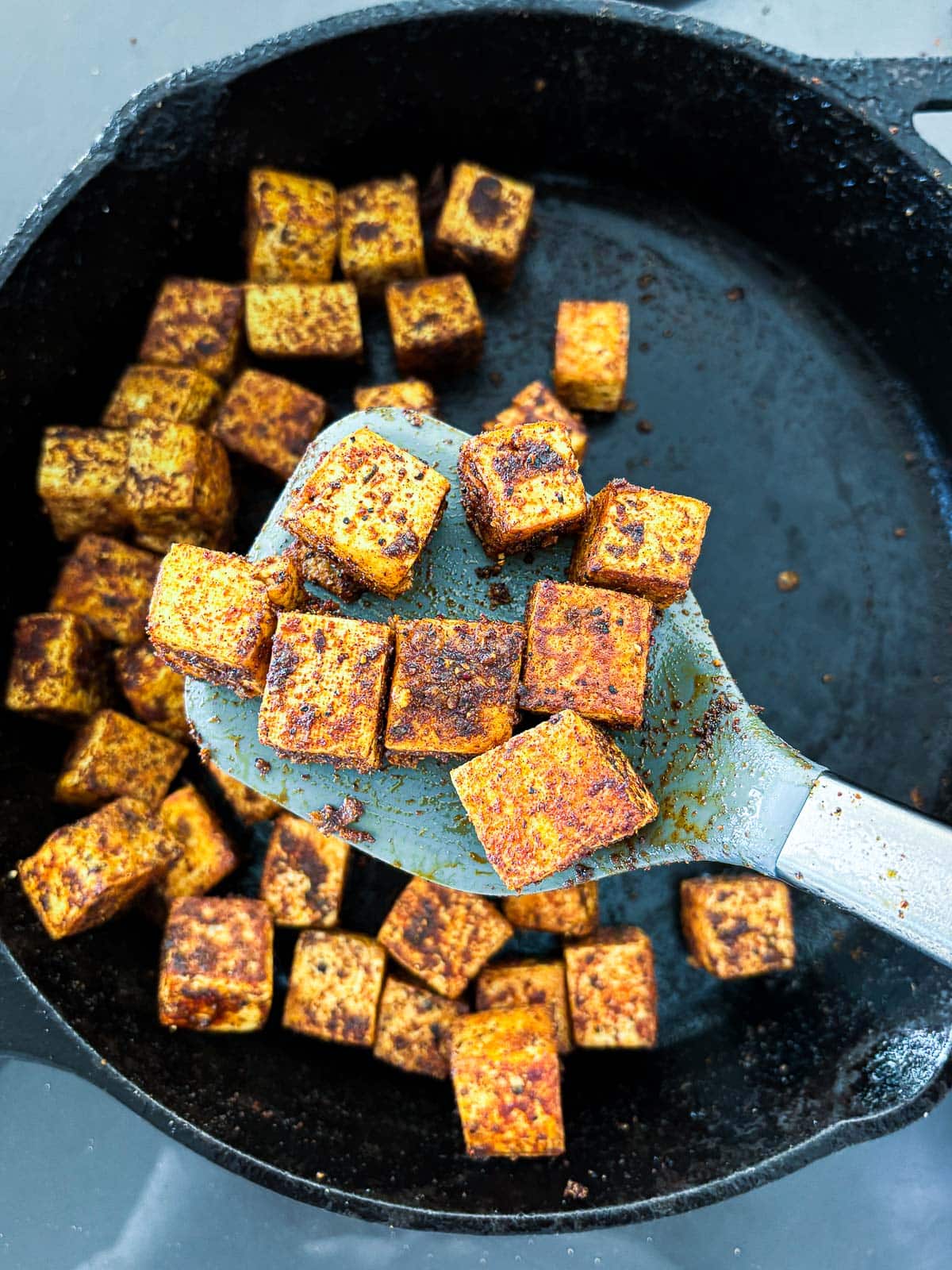 metal spatula lifting up jerk seasoned tofu from cast iron skillet.