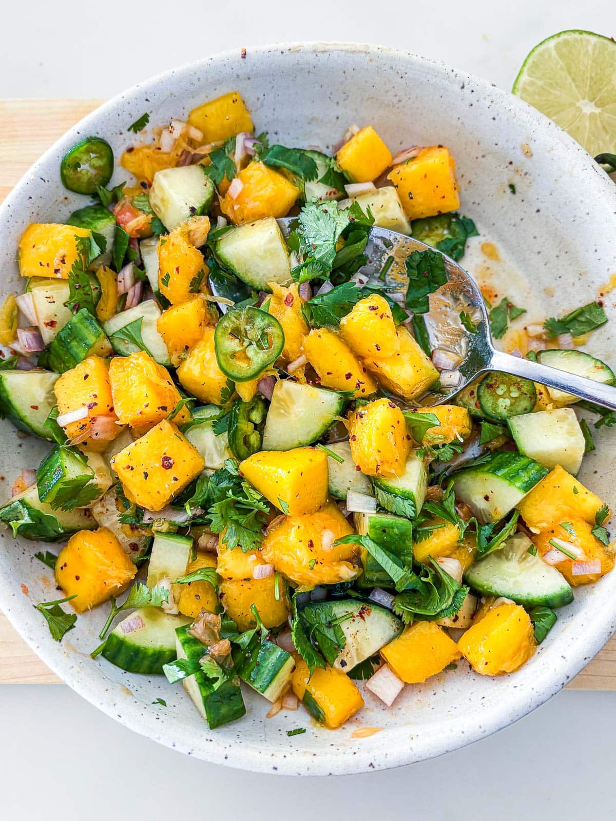 mango salad in a bowl with spoon with cucumbers, jalapeño, and herbs.