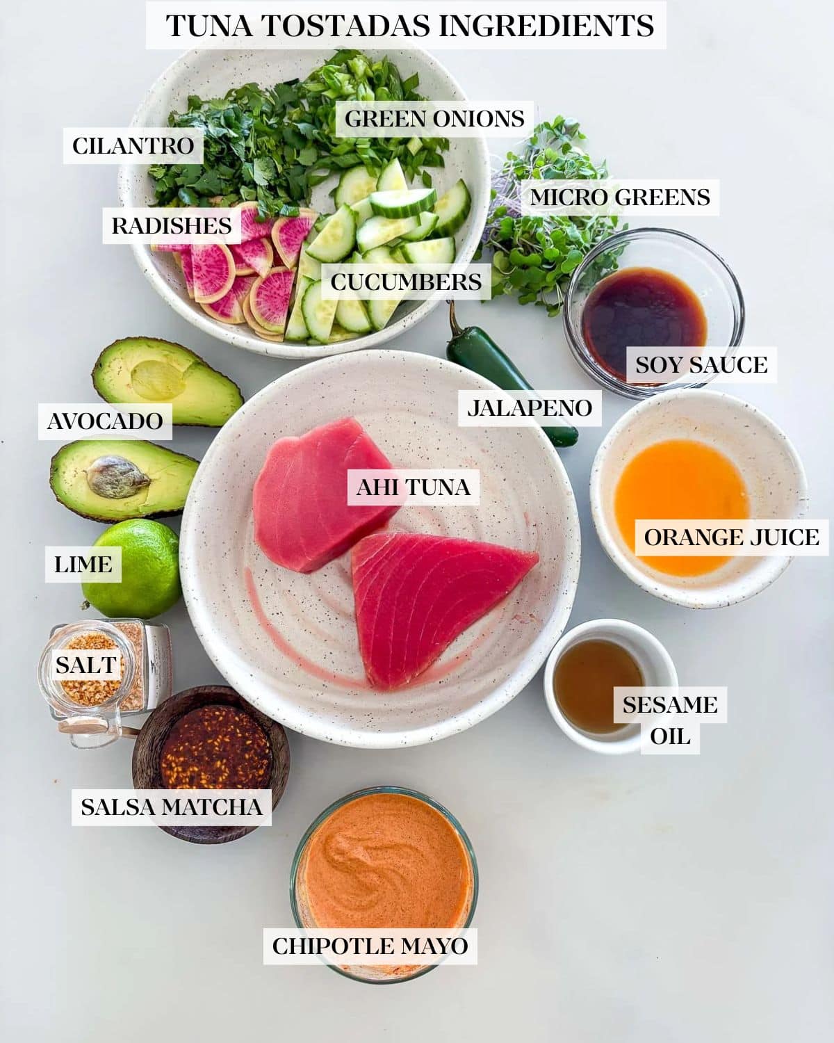 tuna tostadas ingredients arranged neatly in bowls - herbs, radish and cucumber slices, microgreens, soy sauce, orange juice, sesame oil, jalapeno, chipotle mayo, salsa macha, lime, and avocado surrounding bowl of ahi tuna.