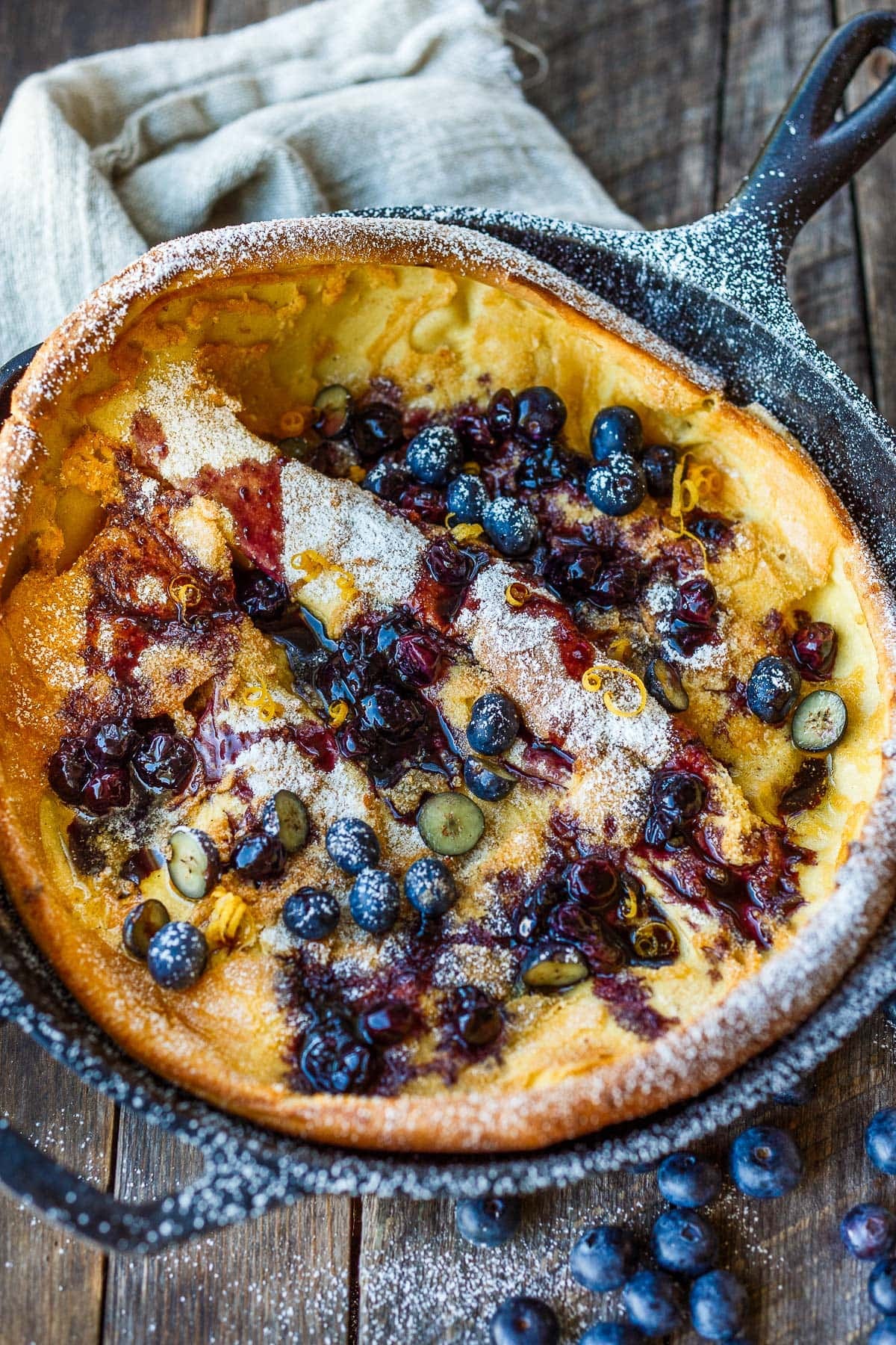 dutch baby with powdered sugar, blueberries, lemon zest, and blueberry sauce. 