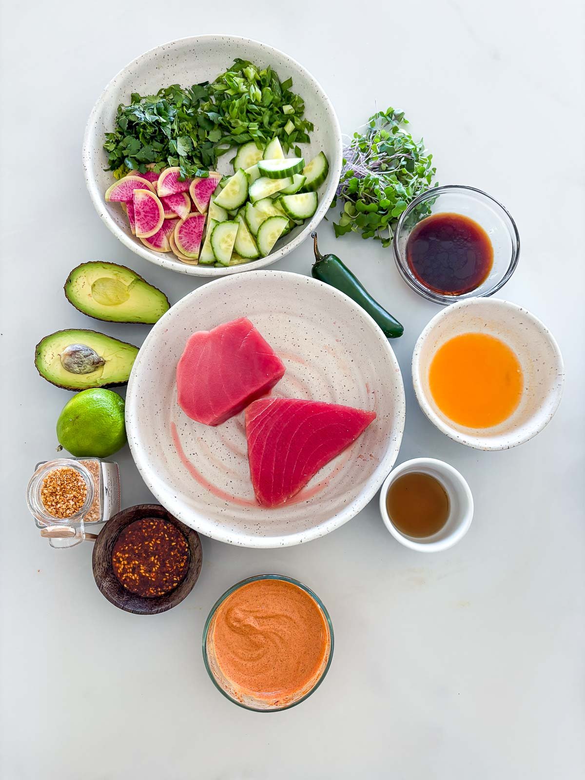 tuna tostadas ingredients arranged neatly in bowls - herbs, radish and cucumber slices, microgreens, soy sauce, orange juice, sesame oil, jalapeno, chipotle mayo, salsa macha, lime, and avocado surrounding bowl of ahi tuna.