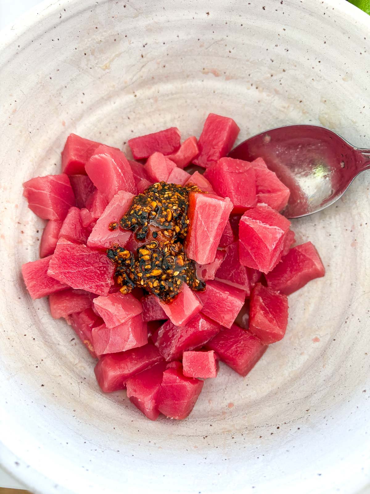 bowl of cubed ahi tuna with salsa macha on top with spoon ready to mix.