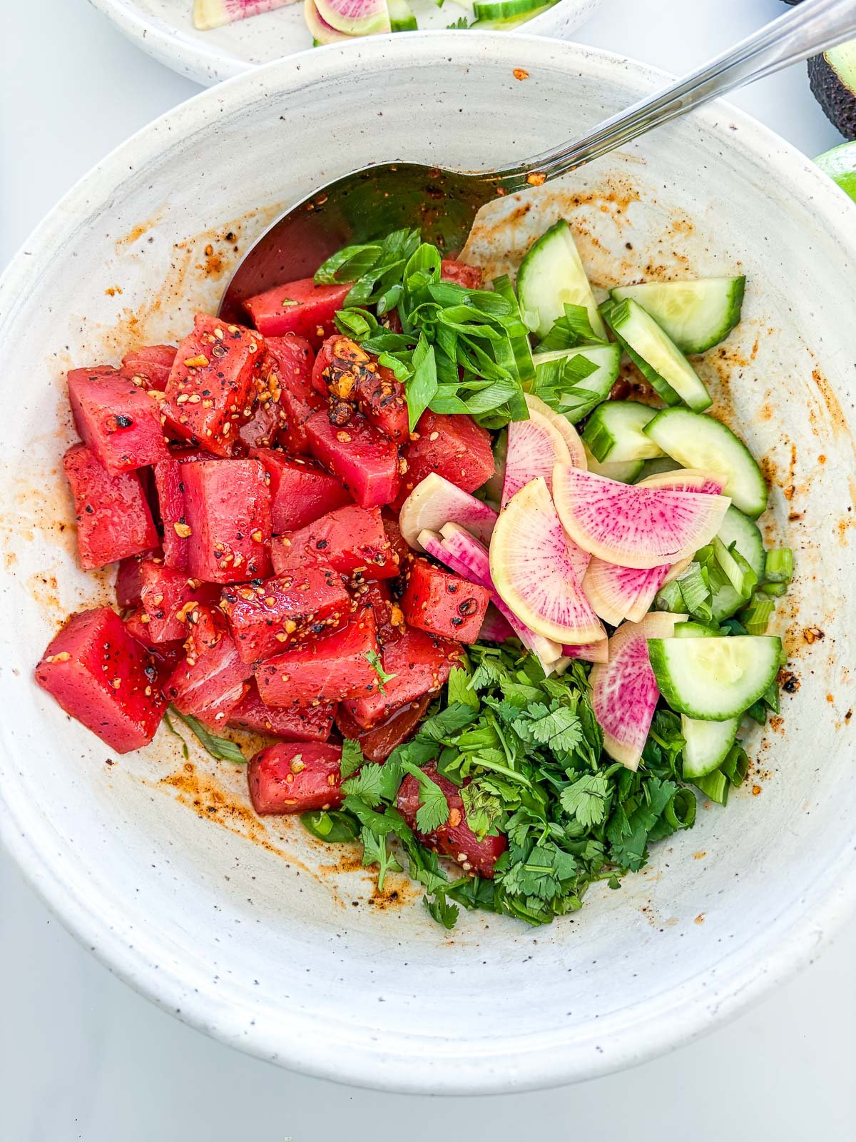 bowl of tuna tostadas ingredients before mixing - ahi tuna, herbs, green onions, sliced cucumbers and radishes, and salsa macha.