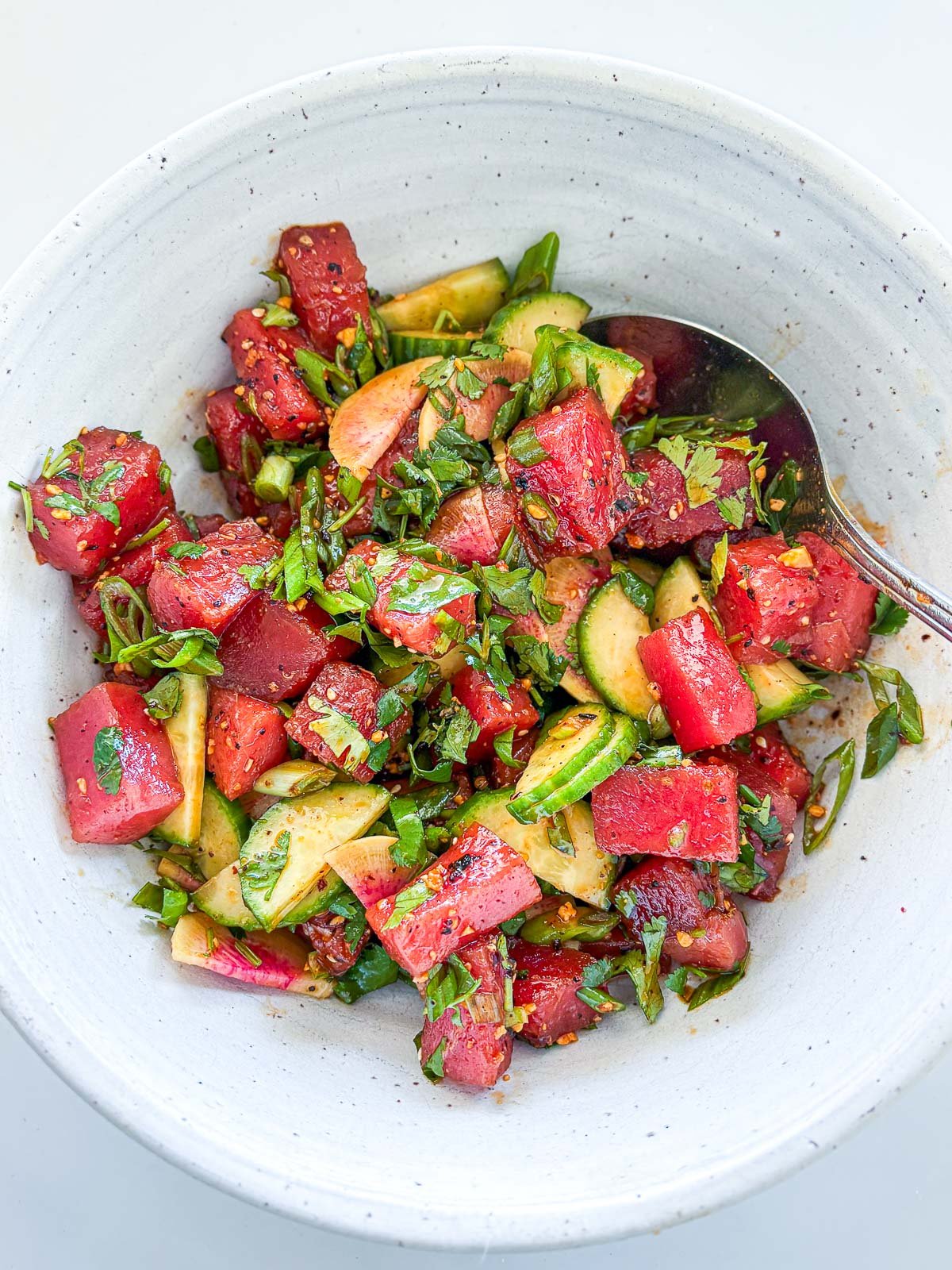bowl of tuna tostadas ingredients mixed together with spoon - ahi tuna, cucumbers, radishes, herbs, and salsa macha.