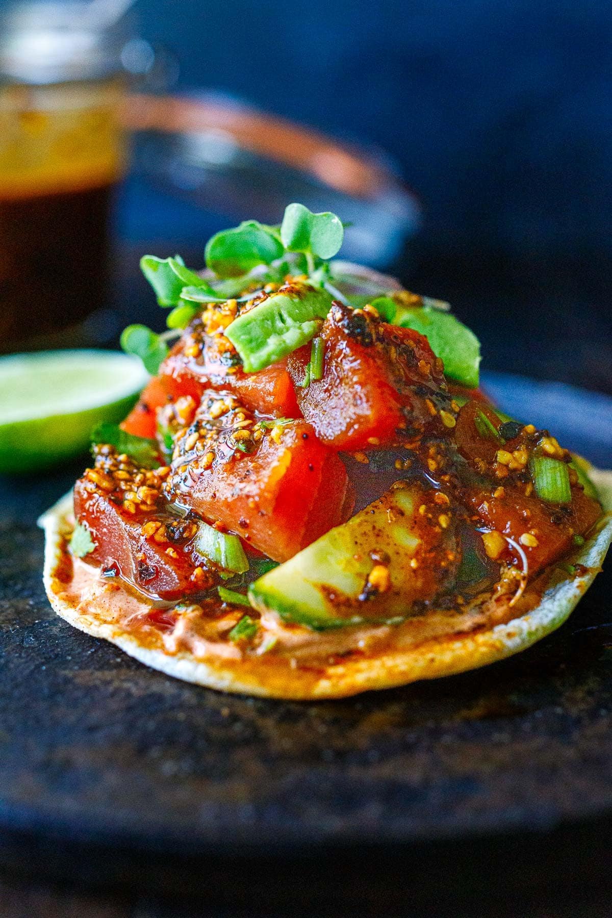 tuna tostada drizzled with salsa macha and topped with cucumber and avocado and microgreens.