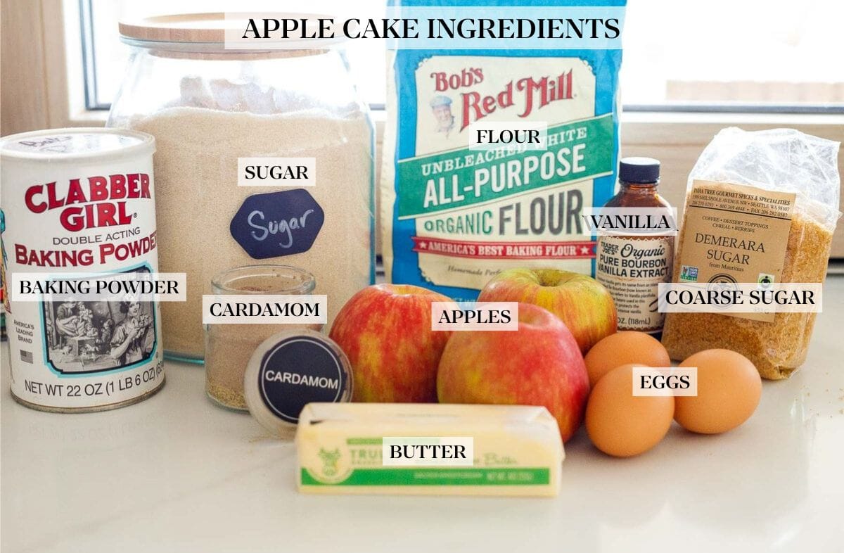 ingredients laid out for apple cake - baking powder, sugar, cardamom, butter, apples, all-purpose flour, vanilla, demerara, eggs.