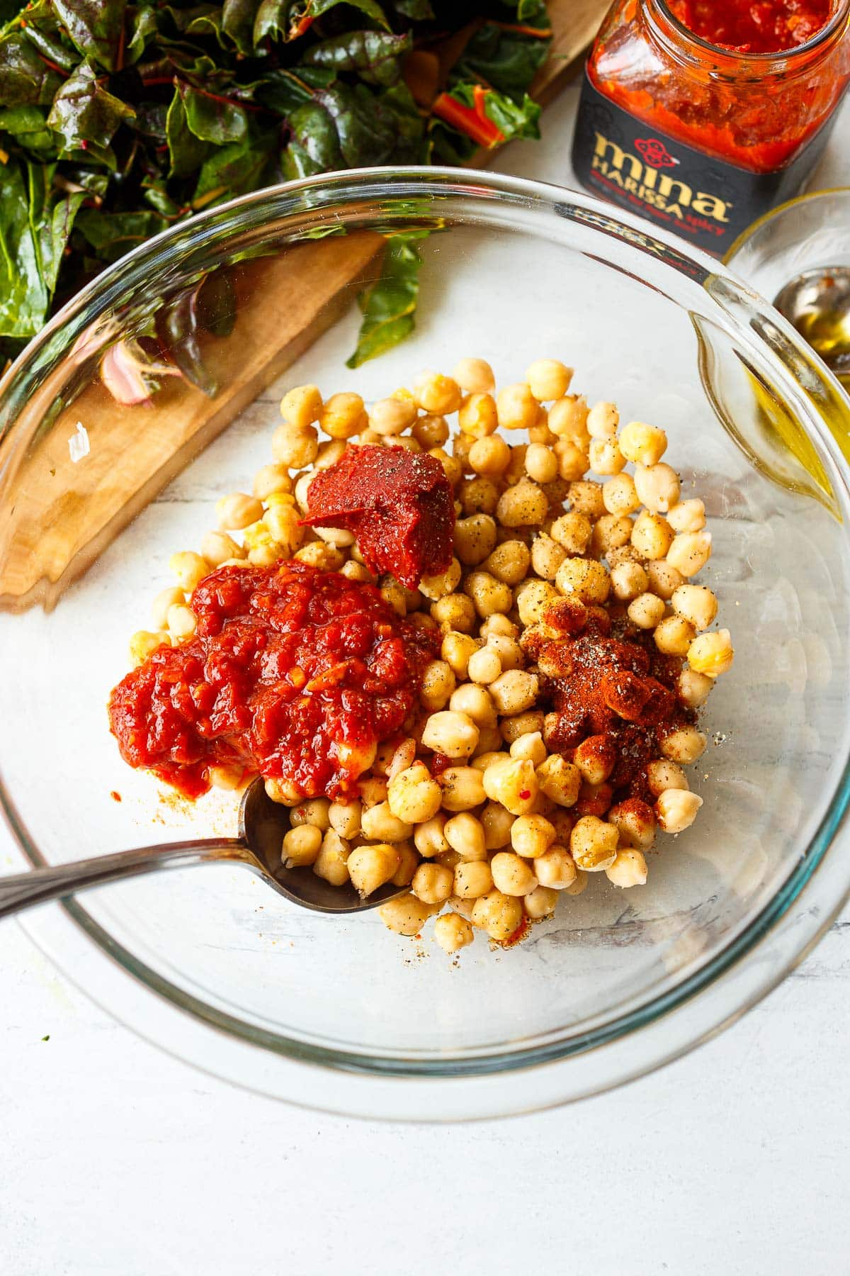 mixing chickpeas with harissa, tomato paste, and smoked paprika in a glass mixing bowl.