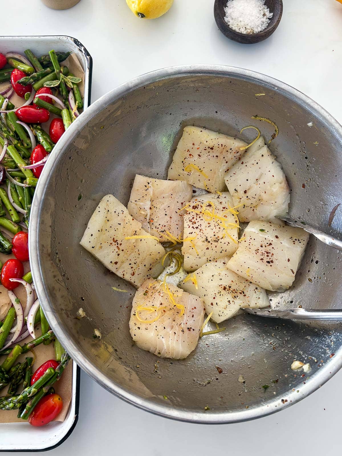 mixing bowl with tongs tossing cod with olive oil, pepper and lemon zest.
