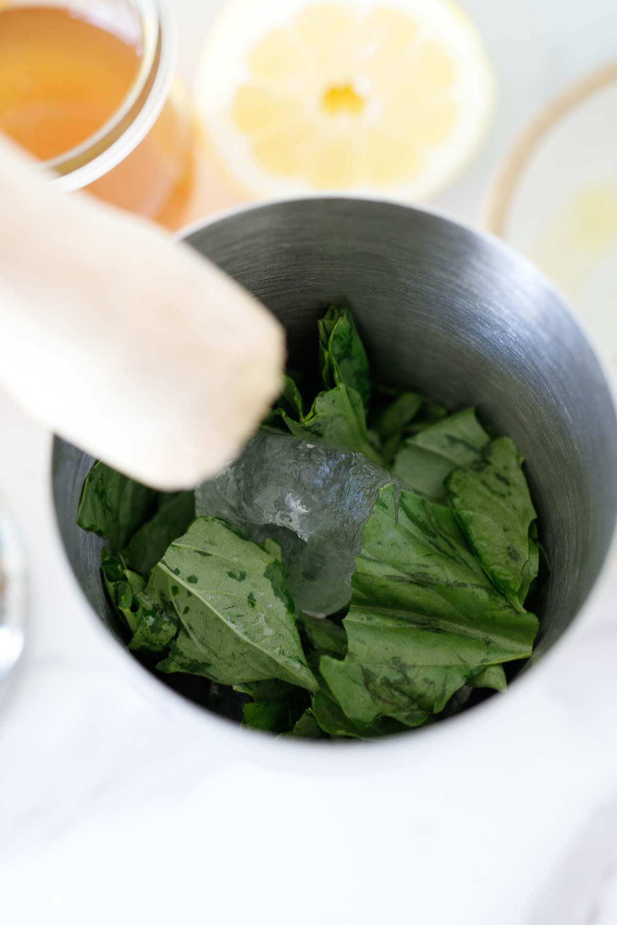 shaker with ice and fresh basil, ready to muddle.