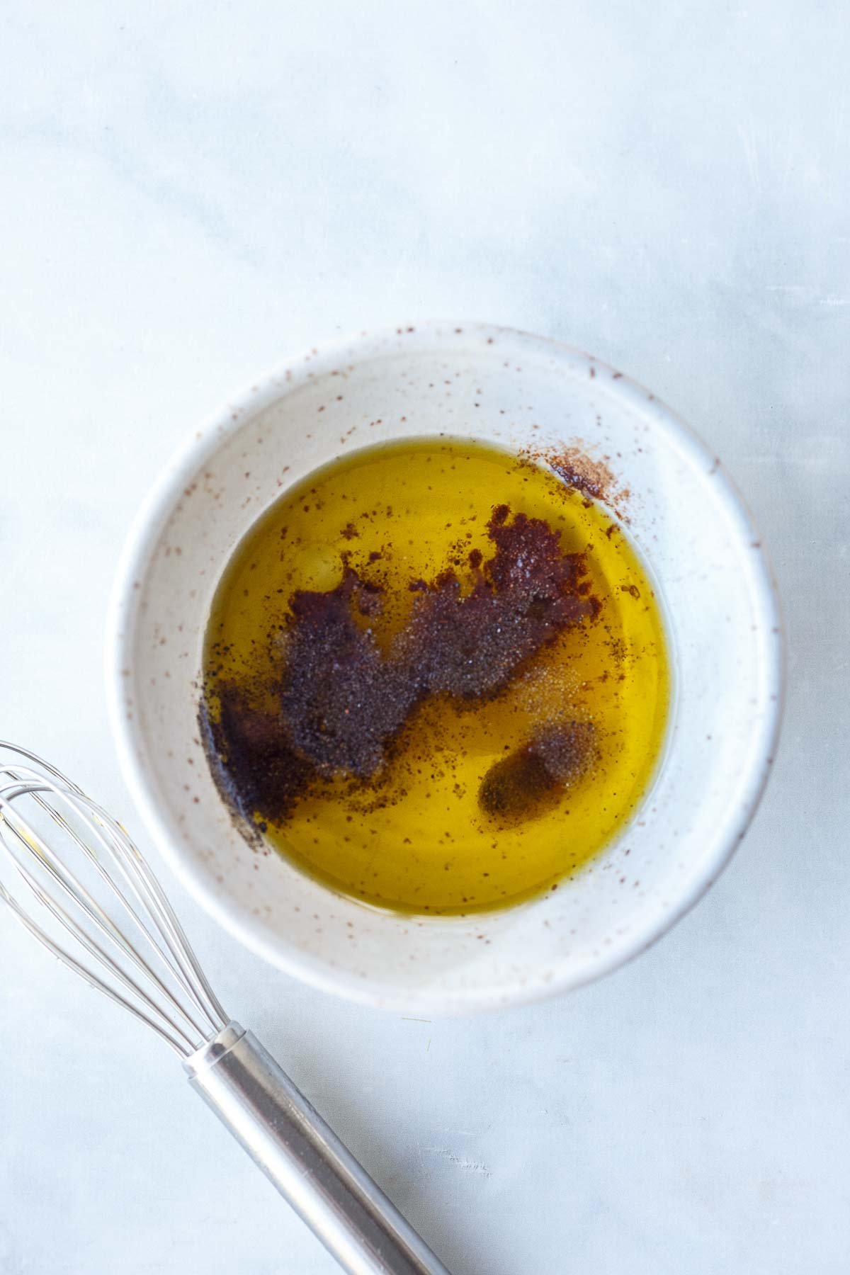 small bowl with silver whisk to the side - with olive oil, white balsamic, and cinnamon.