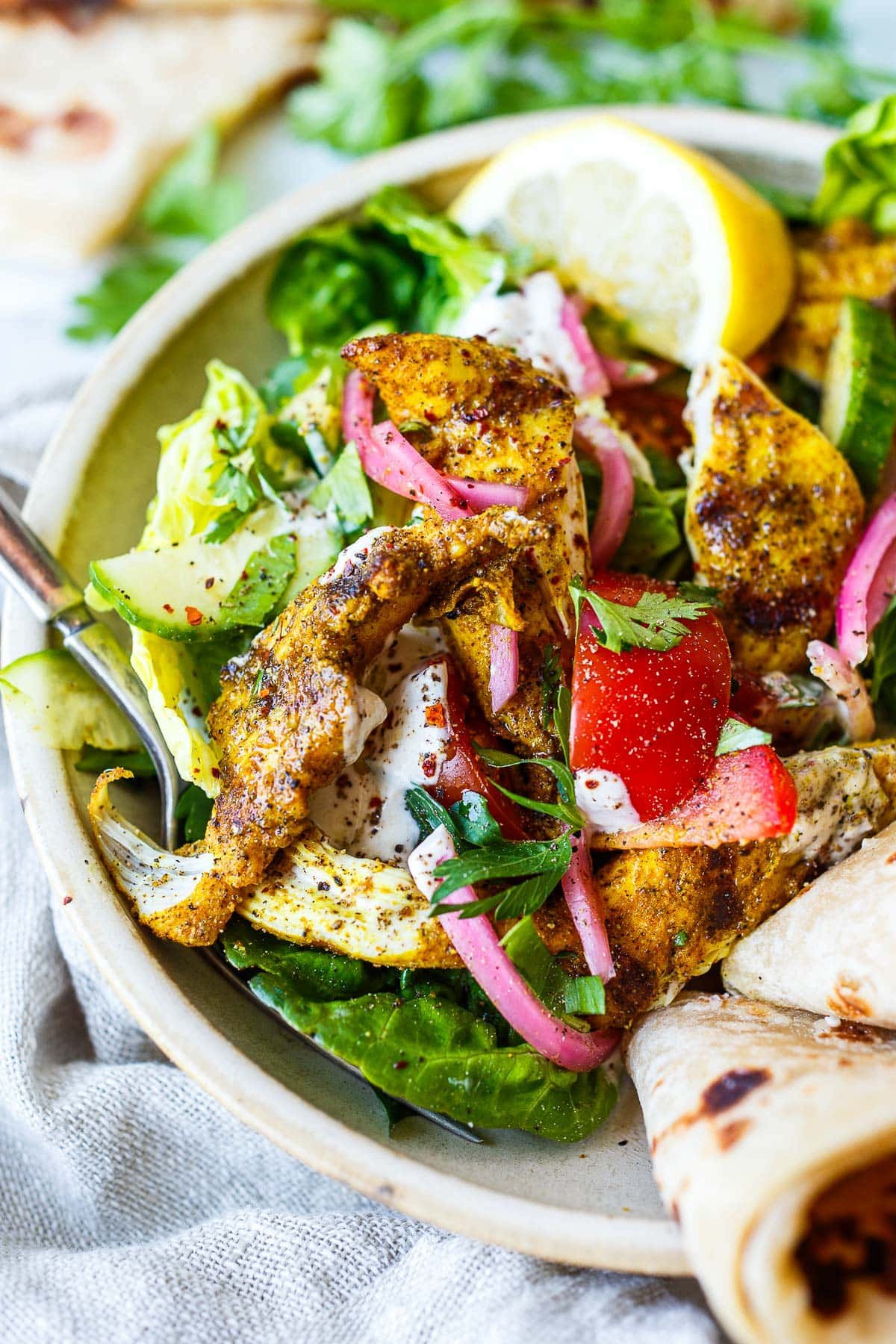 Grilled chicken salad with shawarma spices! Make with little gem lettuce, tomatoes, cucumbers, pickled onions, cilantro, tahini yogurt dressing, lemon quarter, and pita. 