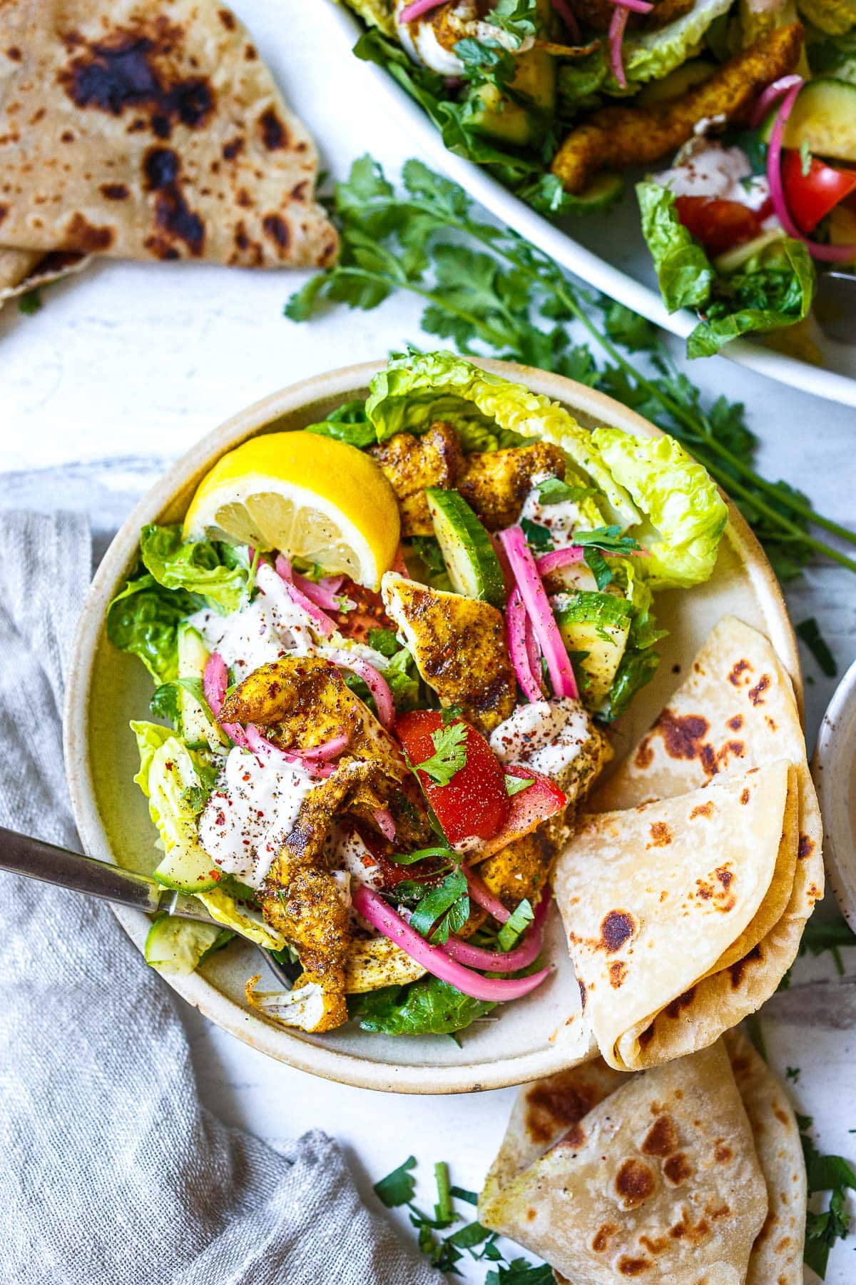 chicken shawarma salad with pickled onions, tomato, cucumber, cilantro, and lemon quarter in bowl with folded naan. 