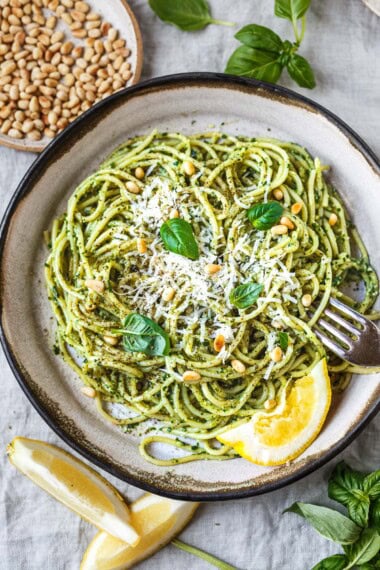 bowl with pesto pasta topped with pine nuts, parmesan, fresh basil, and lemon.