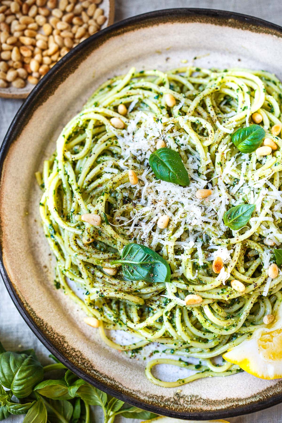 bowl with pesto pasta topped with pine nuts, parmesan, fresh basil, and lemon.