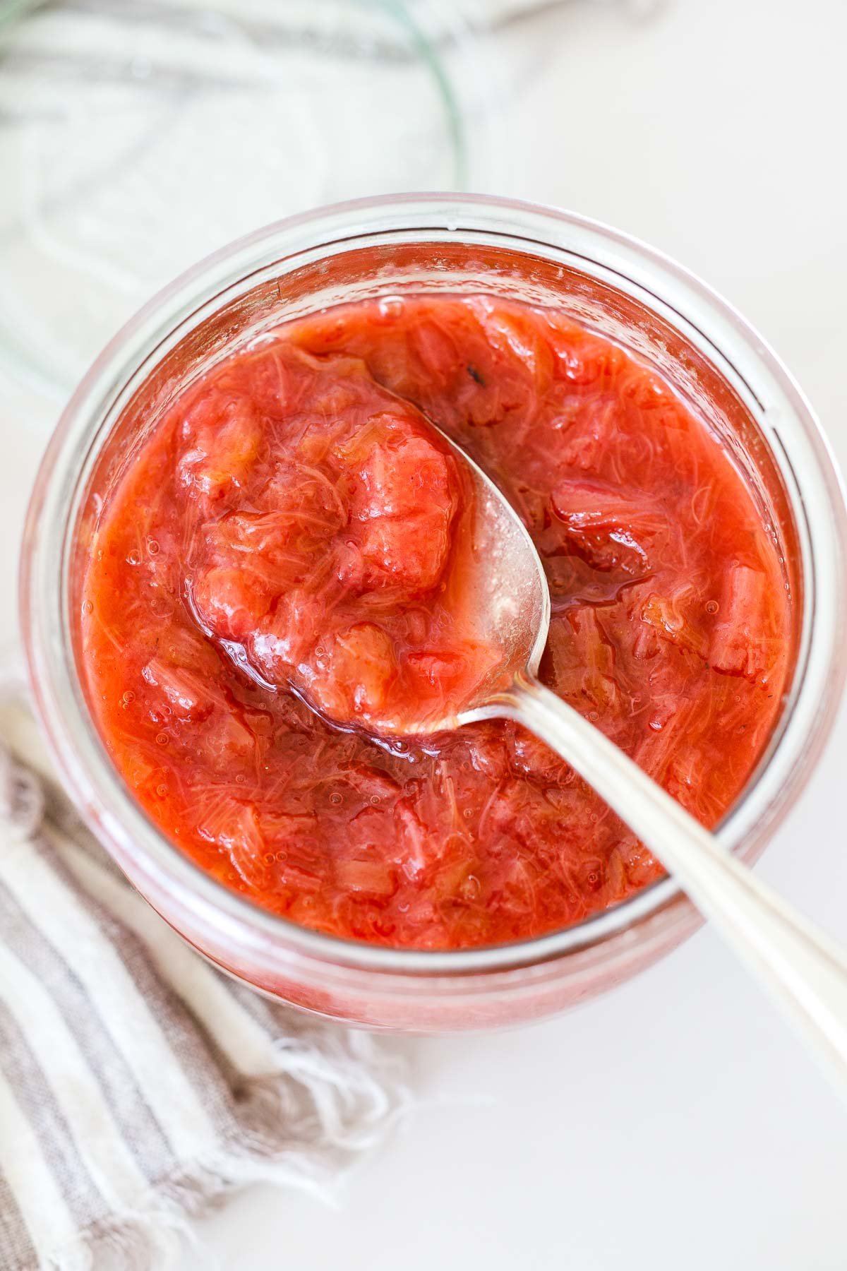 glass jar of rhubarb compote with silver spoon lifting a spoonful up over top.