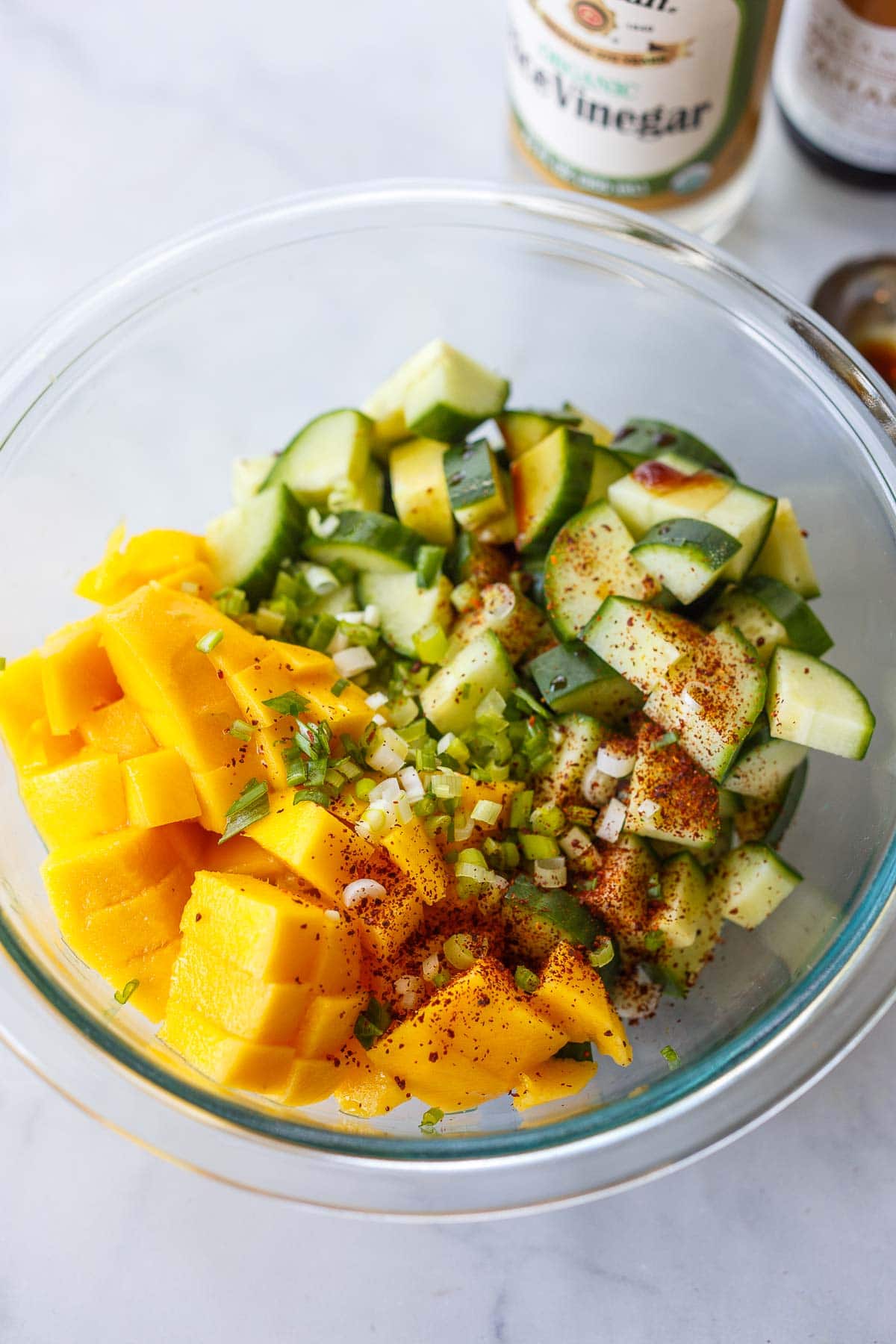 Mango and cucumber in a glass bowl with green onions.