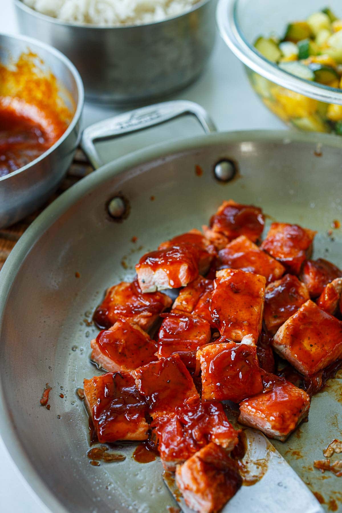 Salmon cubes coated with sticky sauce in a large saute pan.