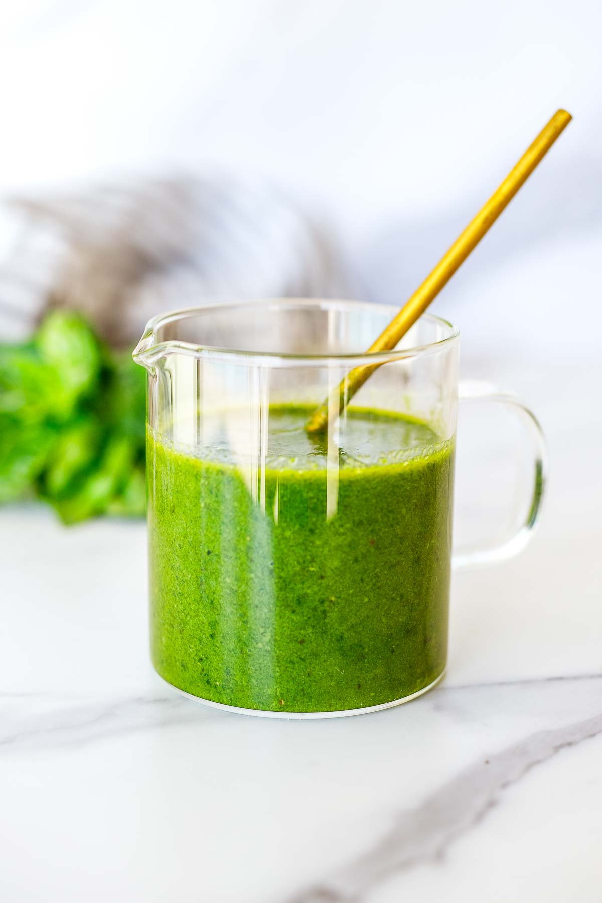 glass jar of basil vinaigrette with gold spoon with fresh basil blurred in the background.