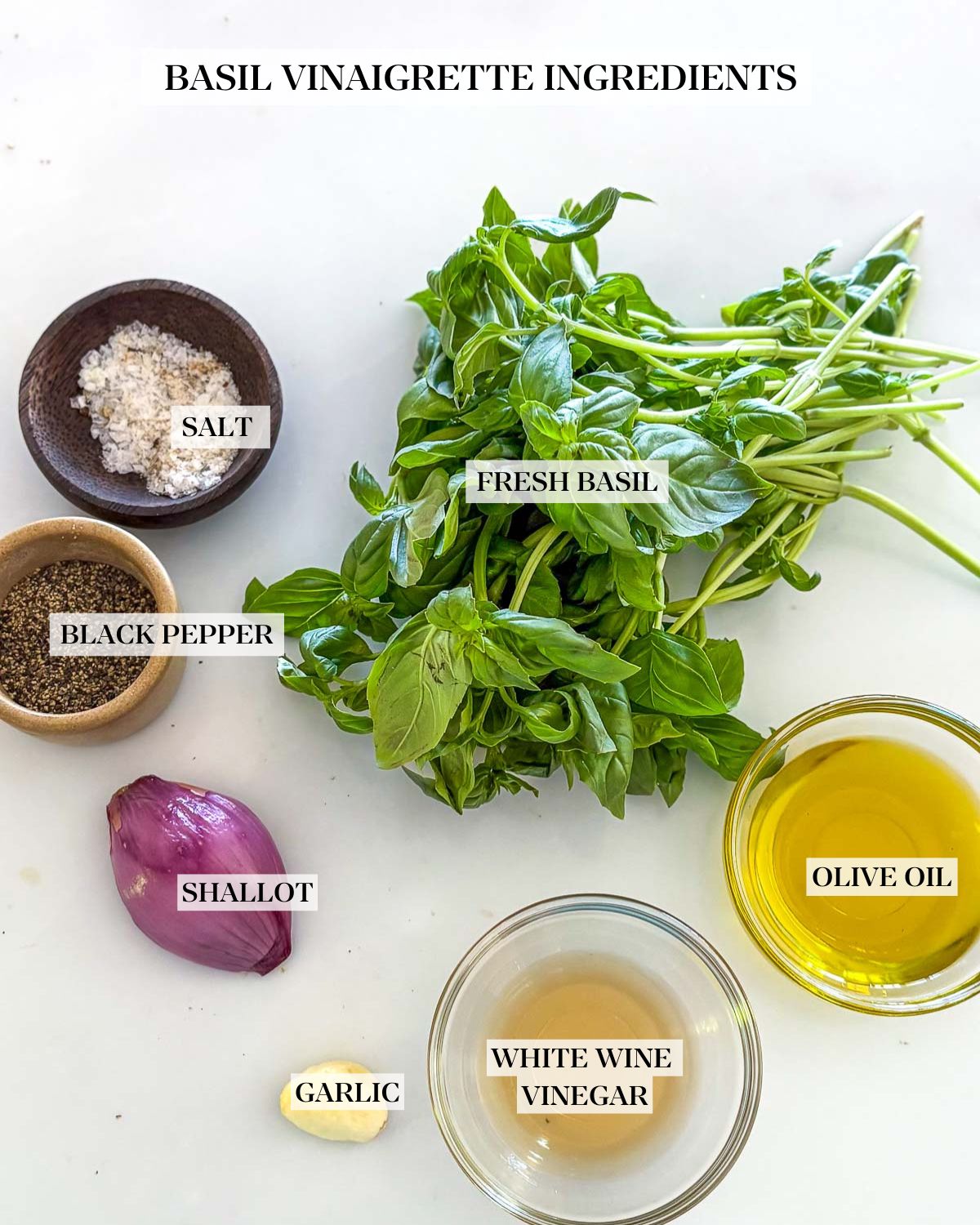 bunch of fresh basil, shallot, garlic clove, and small bowls with salt, pepper, vinegar, and olive oil, arranged neatly to make basil vinaigrette.