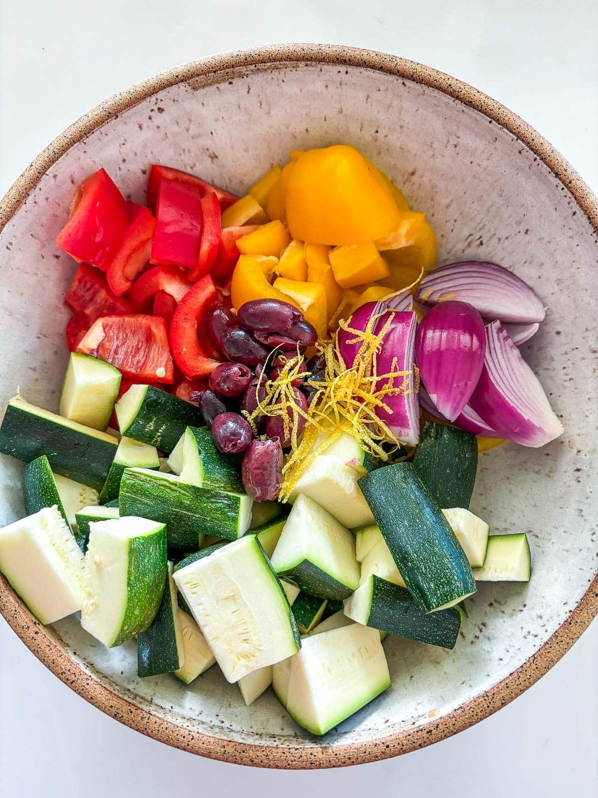 chopped veggies in a bowl with olives, onions, lemon zest and marinade ingredients