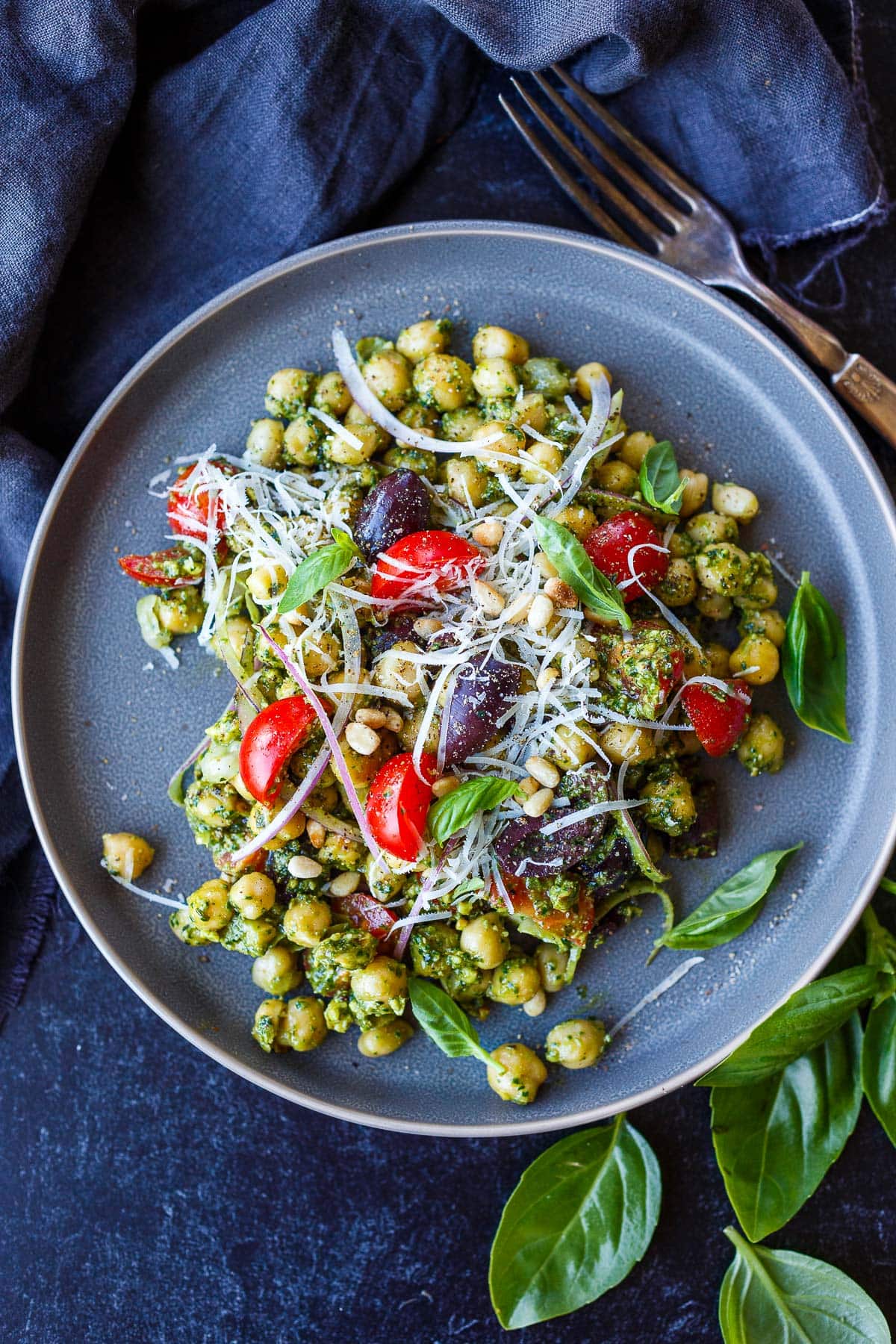 plate of pesto chickpeas with fresh basil, pine nuts, parmesan, olives, and red onion.
