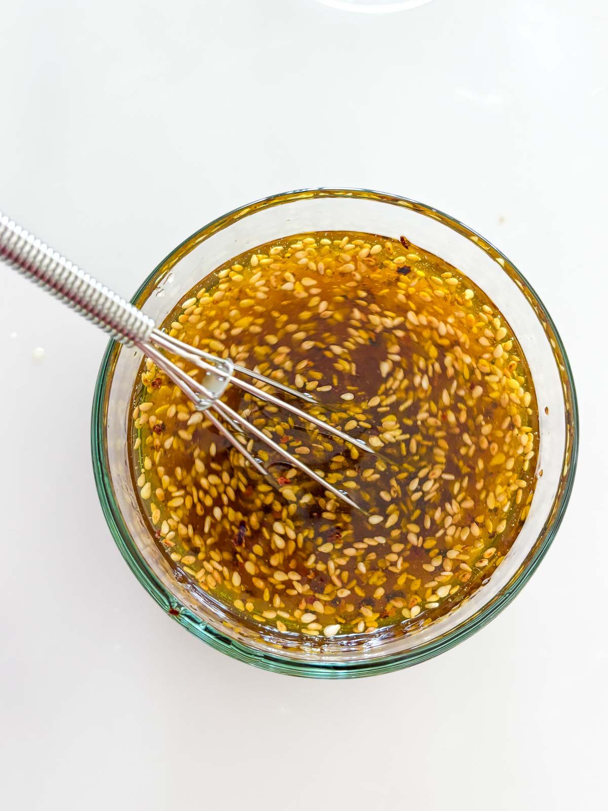 small silver whisk in small glass bowl of sesame ginger dressing.