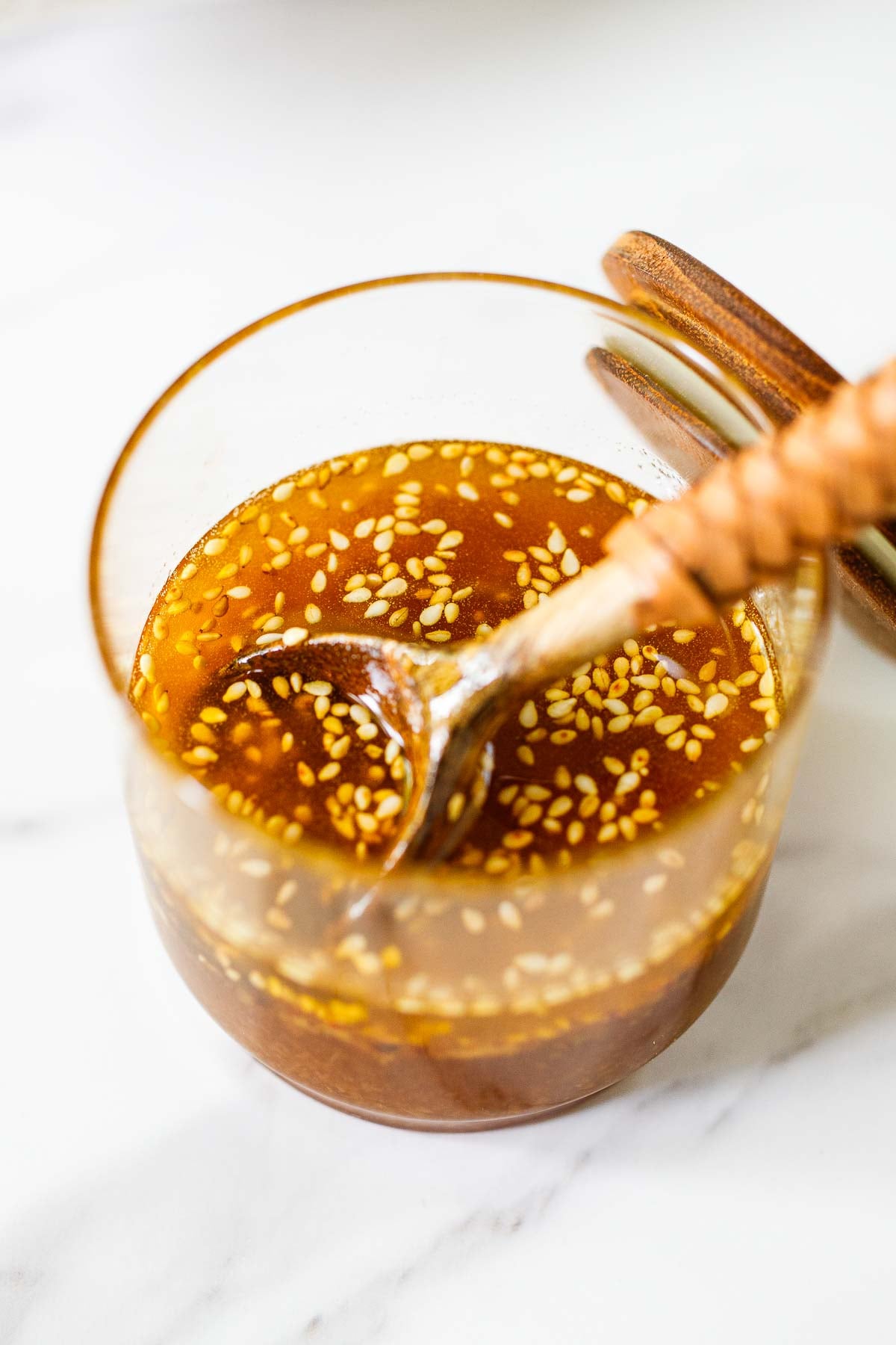 glass jar with sesame ginger dressing with sesame seeds and a wood spoon.