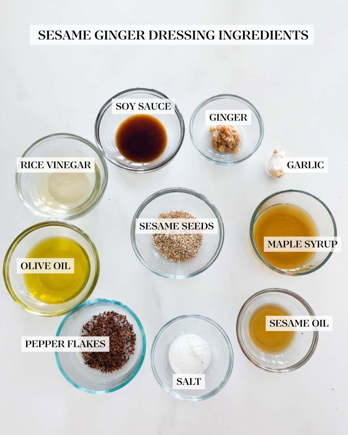 sesame ginger dressing ingredients labeled and arranged neatly in glass bowls - soy sauce, ginger, garlic, maple syrup, sesame oil, salt, pepper flakes, olive oil, rice vinegar, and sesame seeds.