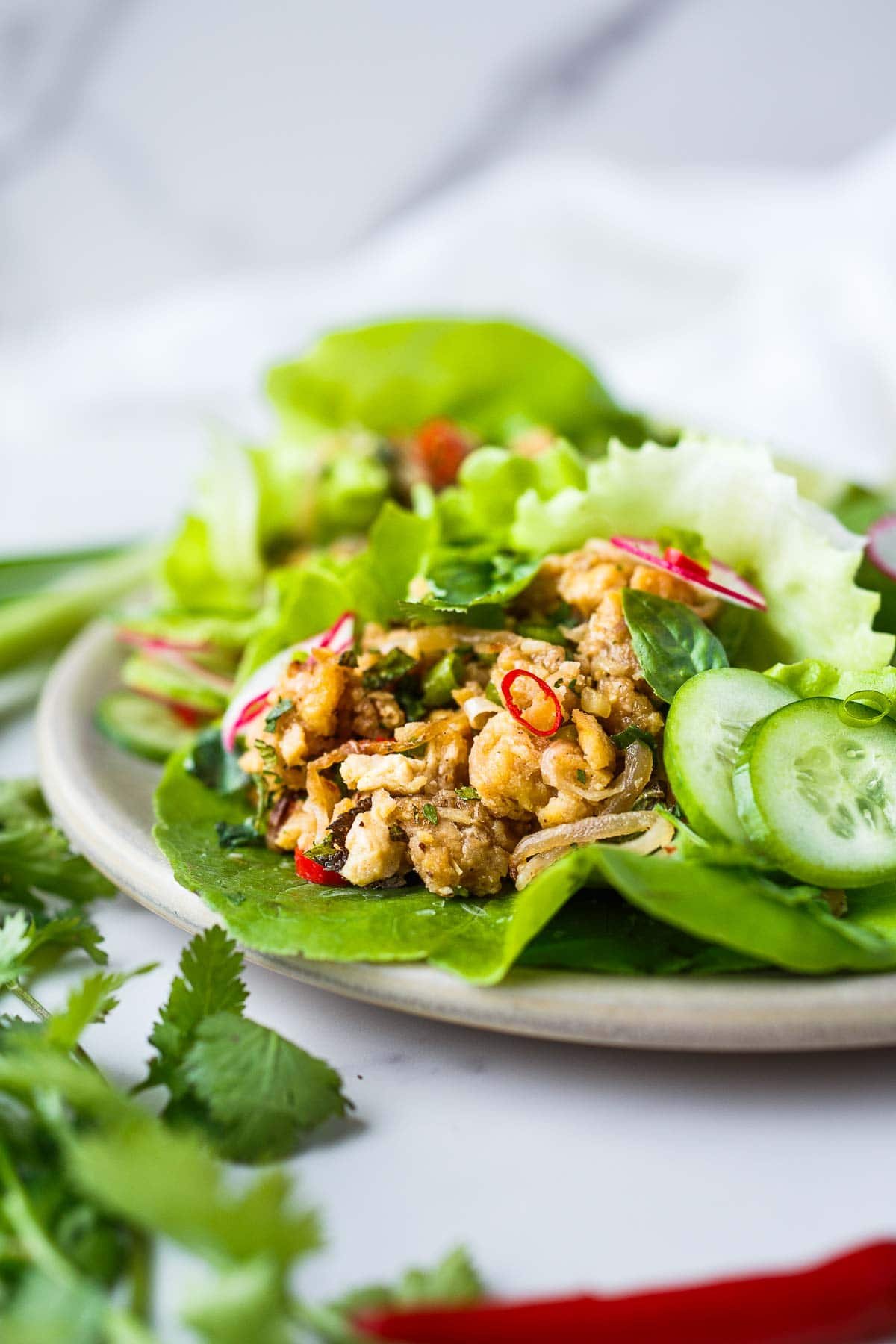 Thai tofu larb in butter lettuce wraps garnished with sliced cucumber and radish and chiles.