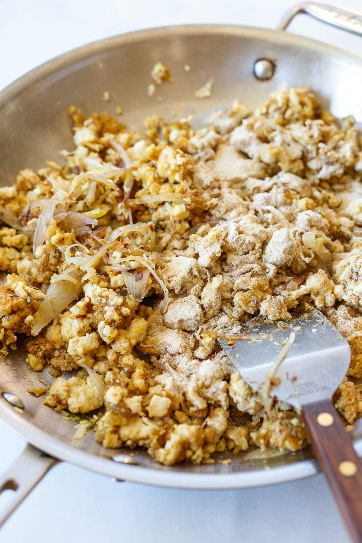 tofu larb in skillet being tossed with toasted rice flour with metal spatula. 