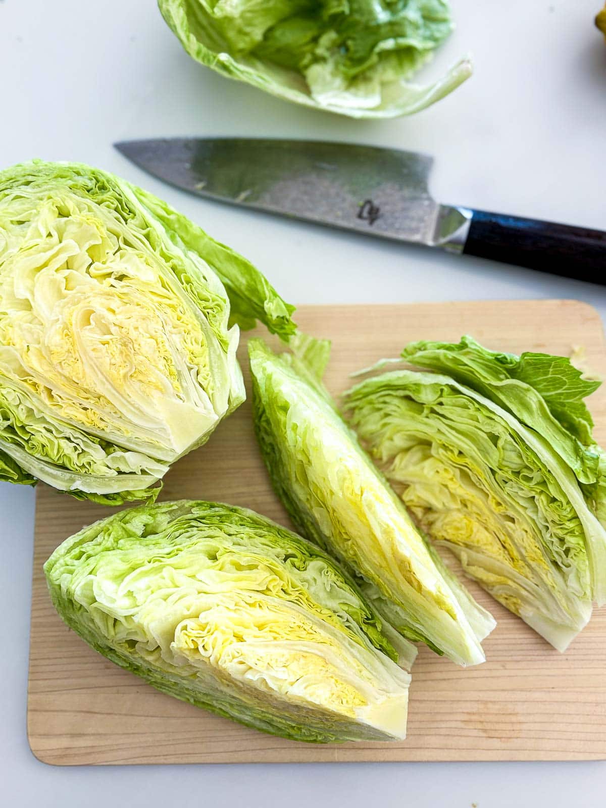 wood cutting board with wedges of iceberg lettuce, next to sharp knife.
